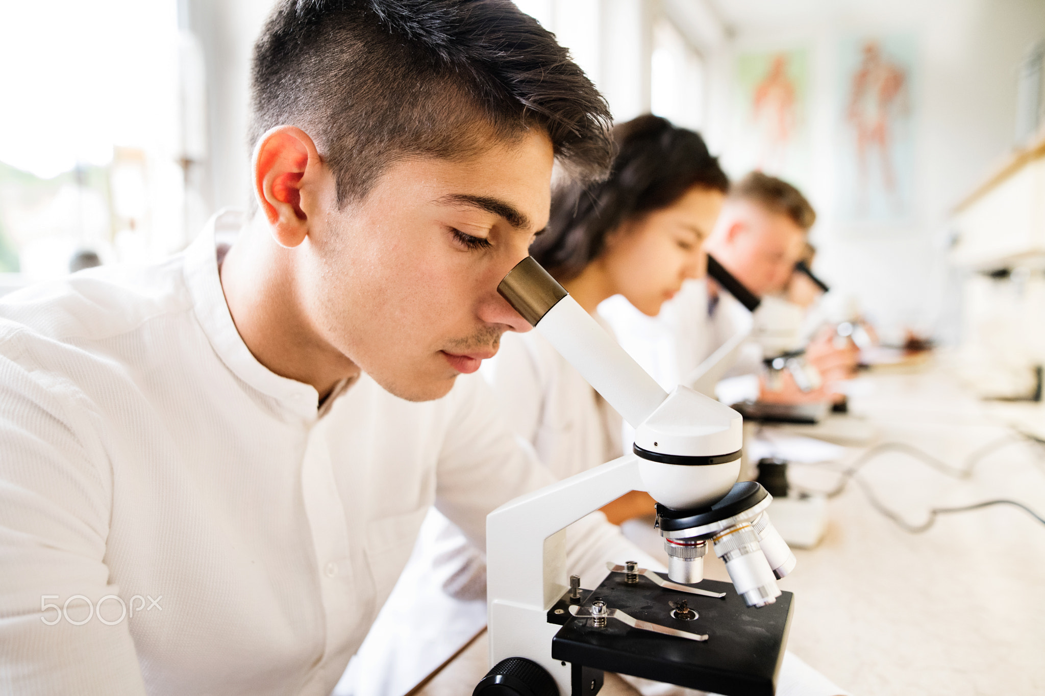 Beautiful high school students with microscopes in laboratory.