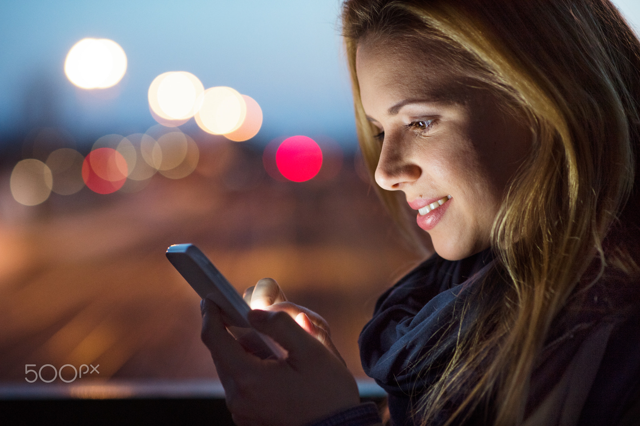 Woman in the city at night holding smartphone, texting.