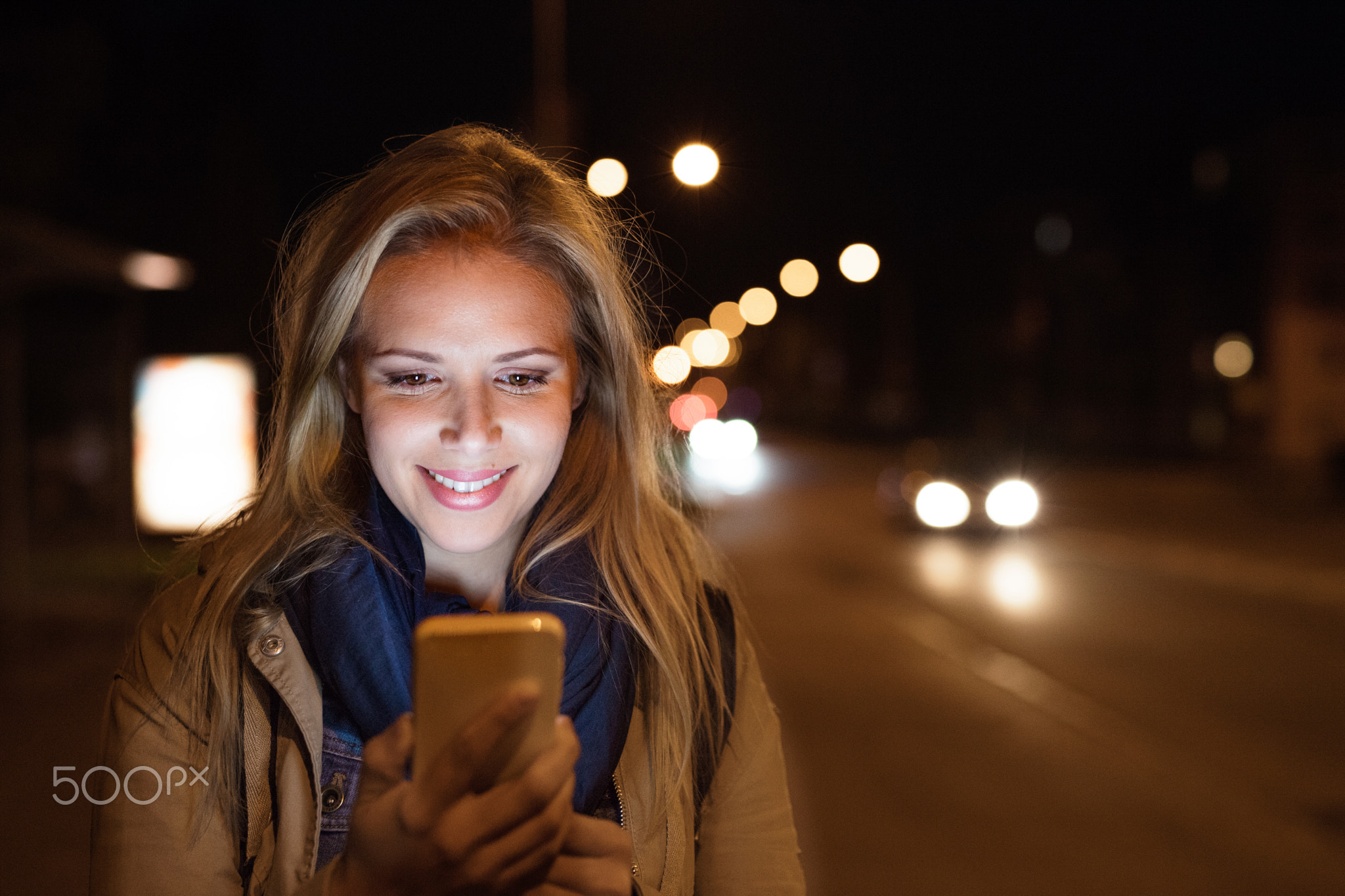 Woman in the city at night holding smartphone, texting.