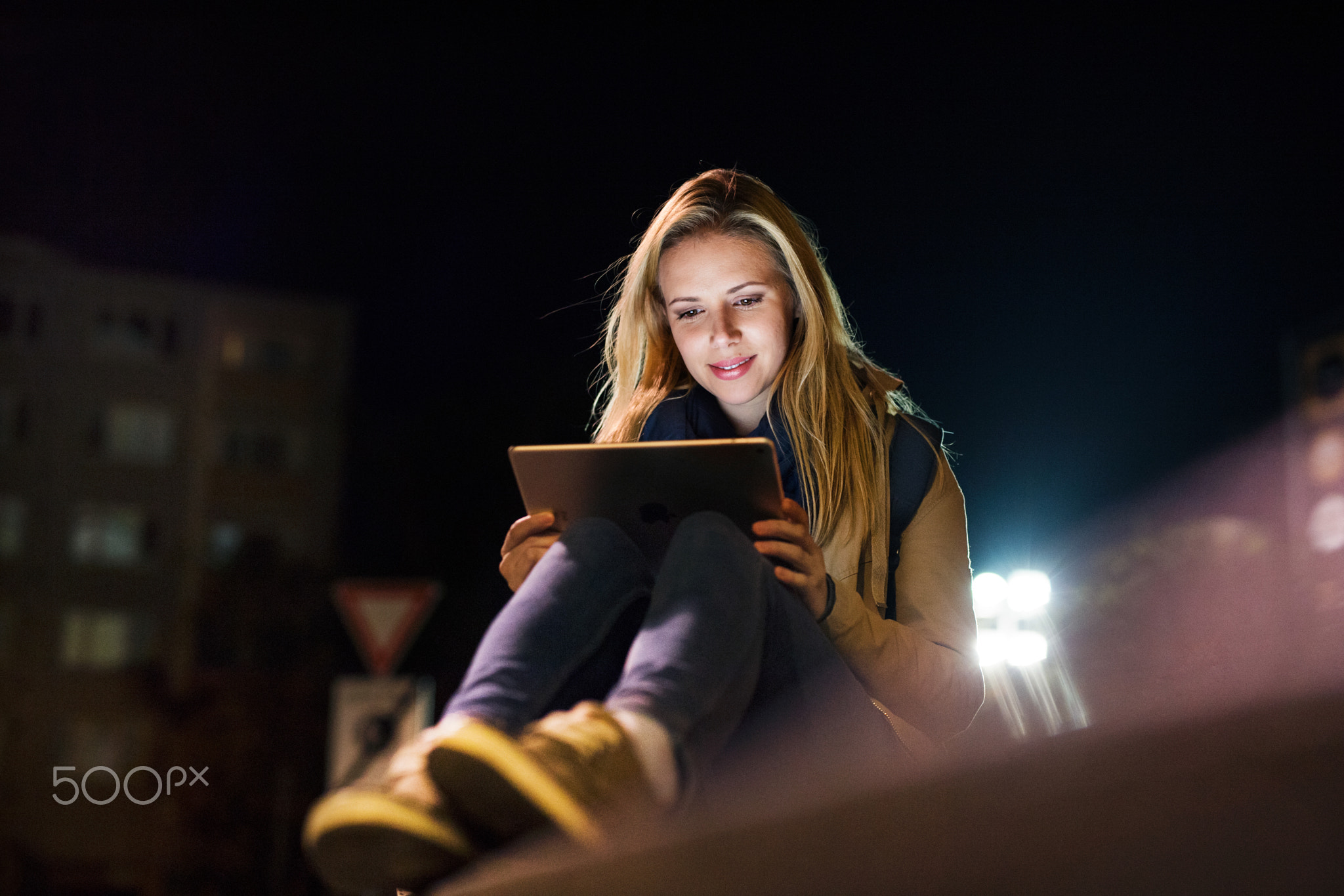 Woman in the city at night holding tablet, reading something.