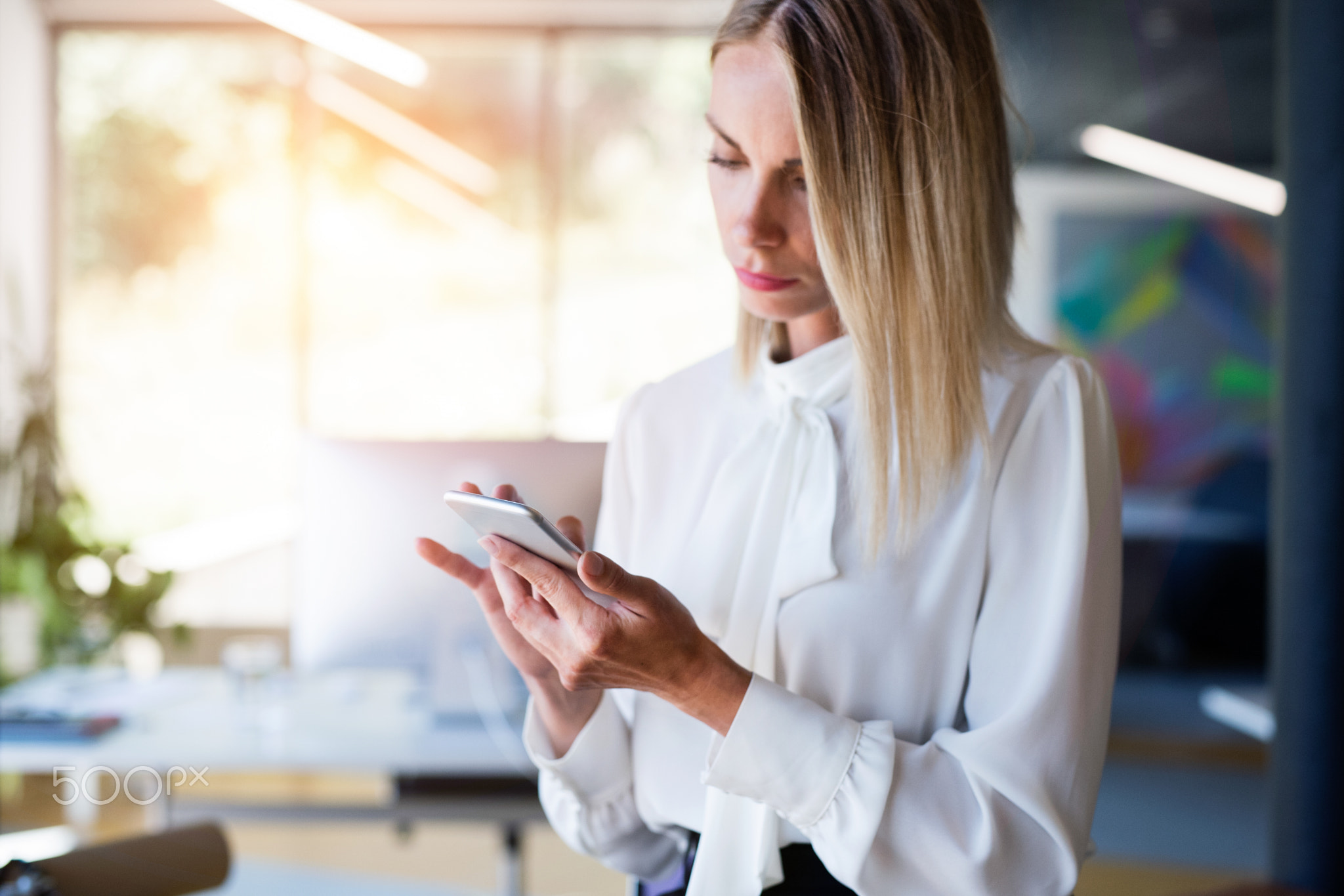 Businesswoman in her office with smartphone texting.