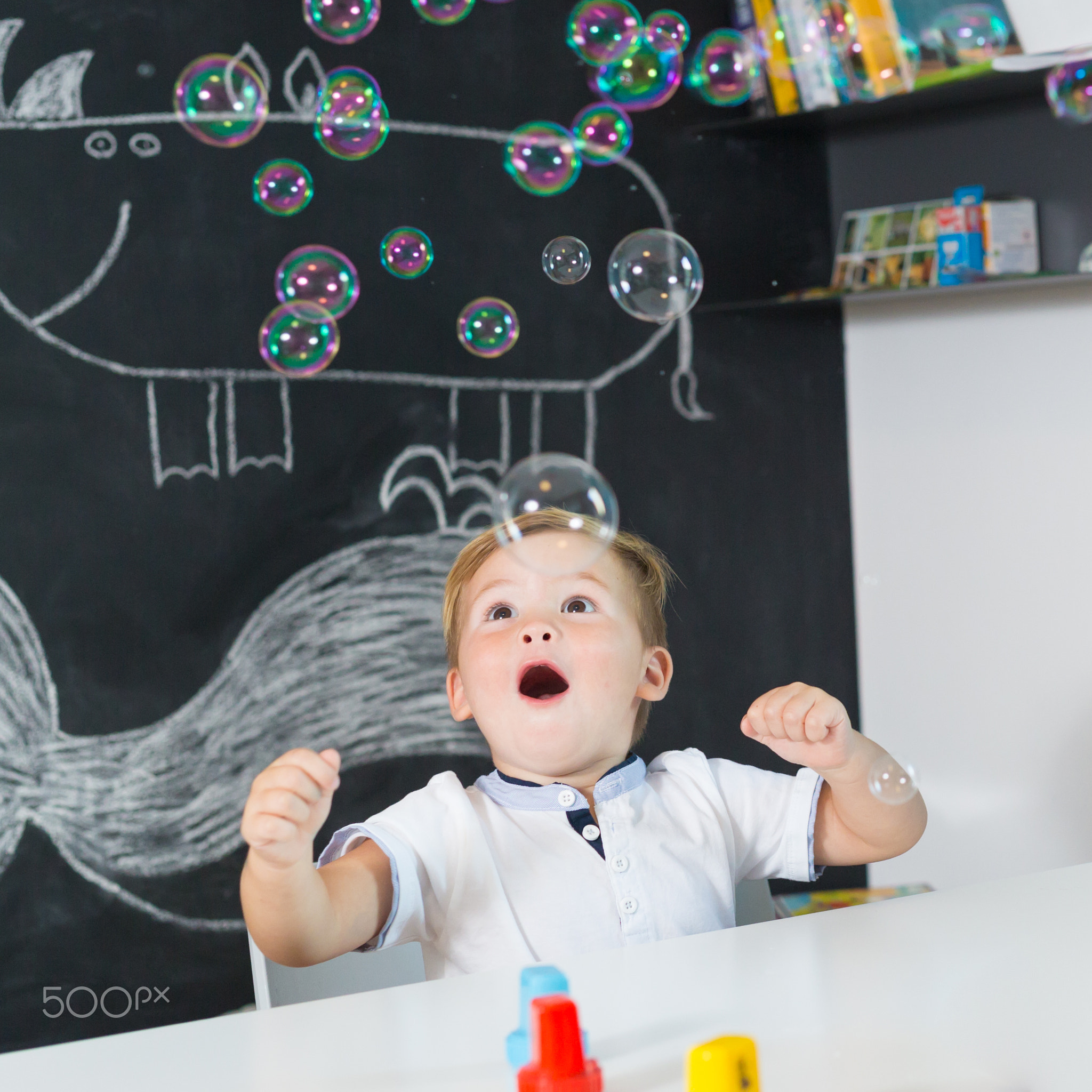 Portrait of cute toddler boy amazed by milky bubbles.