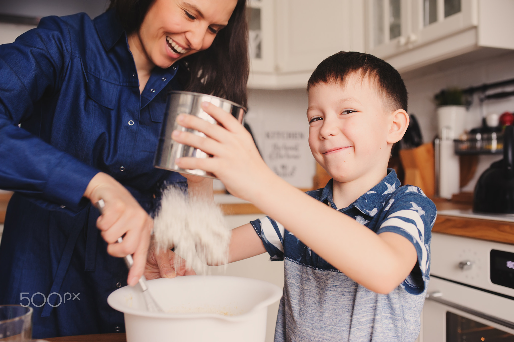 mother and kid son preparing the dough for cookies and pouring flour in the white modern kitchen