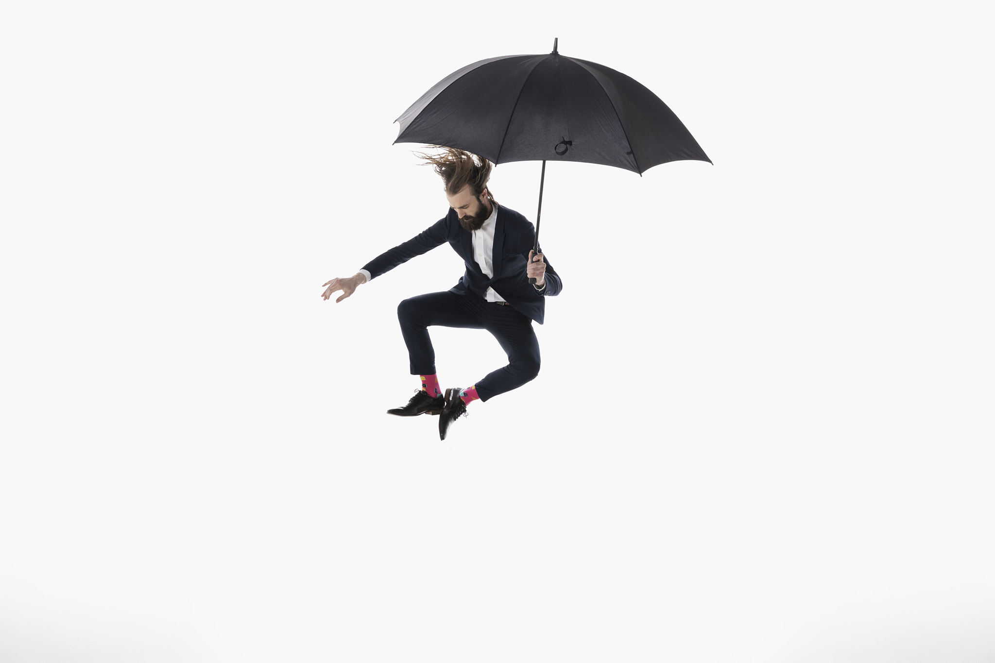 Businessman with umbrella jumping and clicking heels against white background