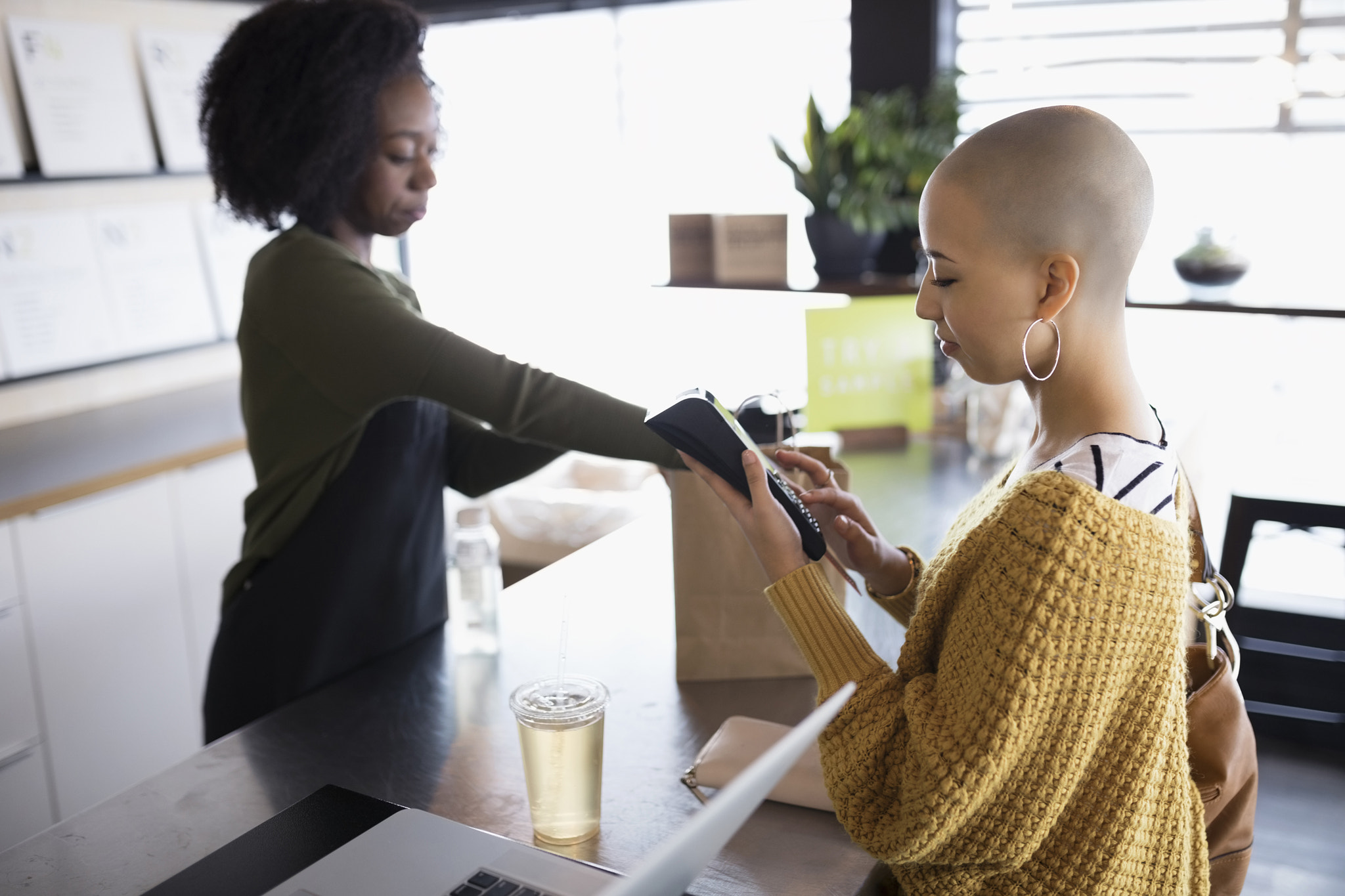 Young woman with shaved head using credit card reader at juice bar