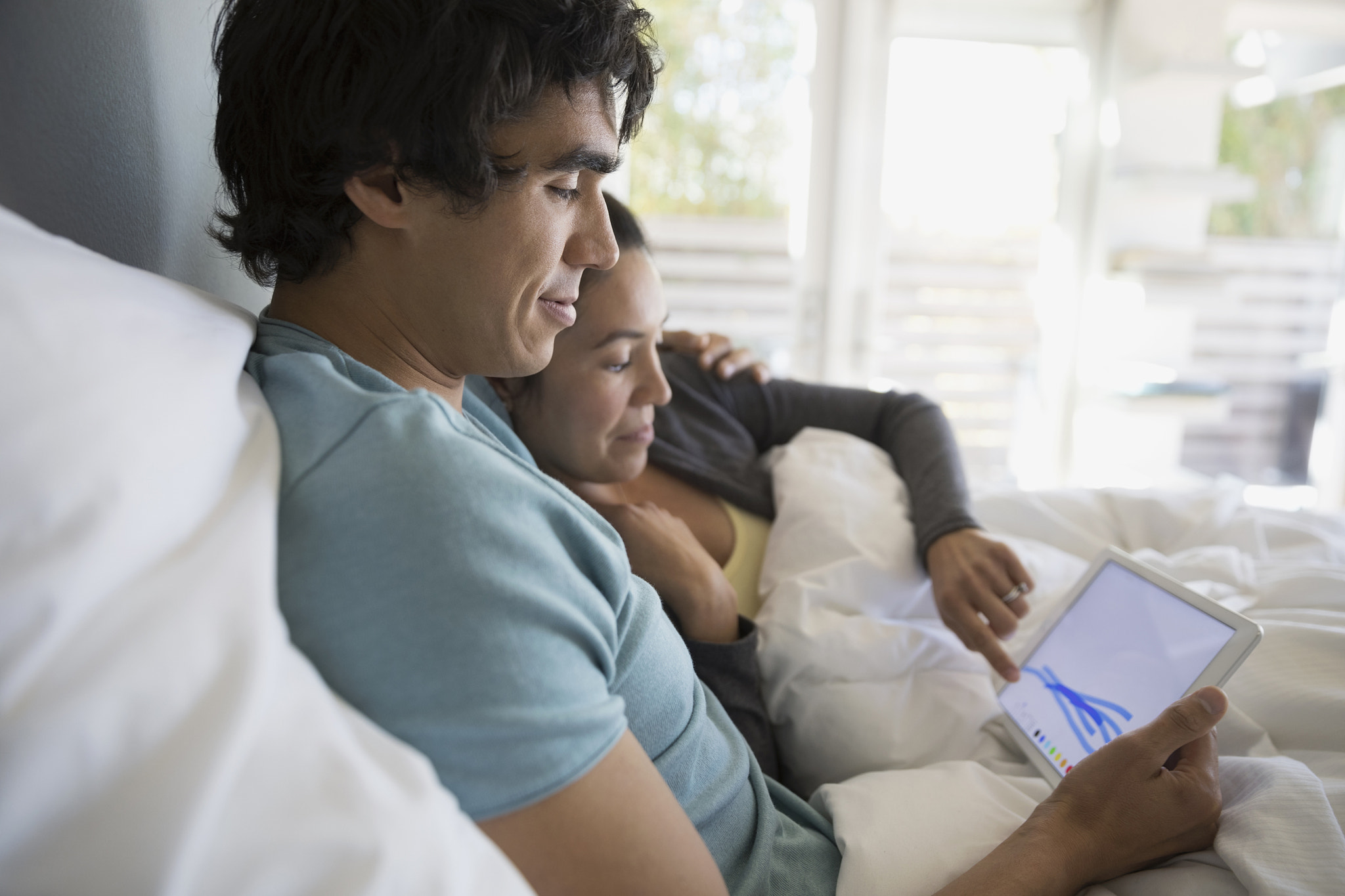 Couple drawing, using digital tablet in bed