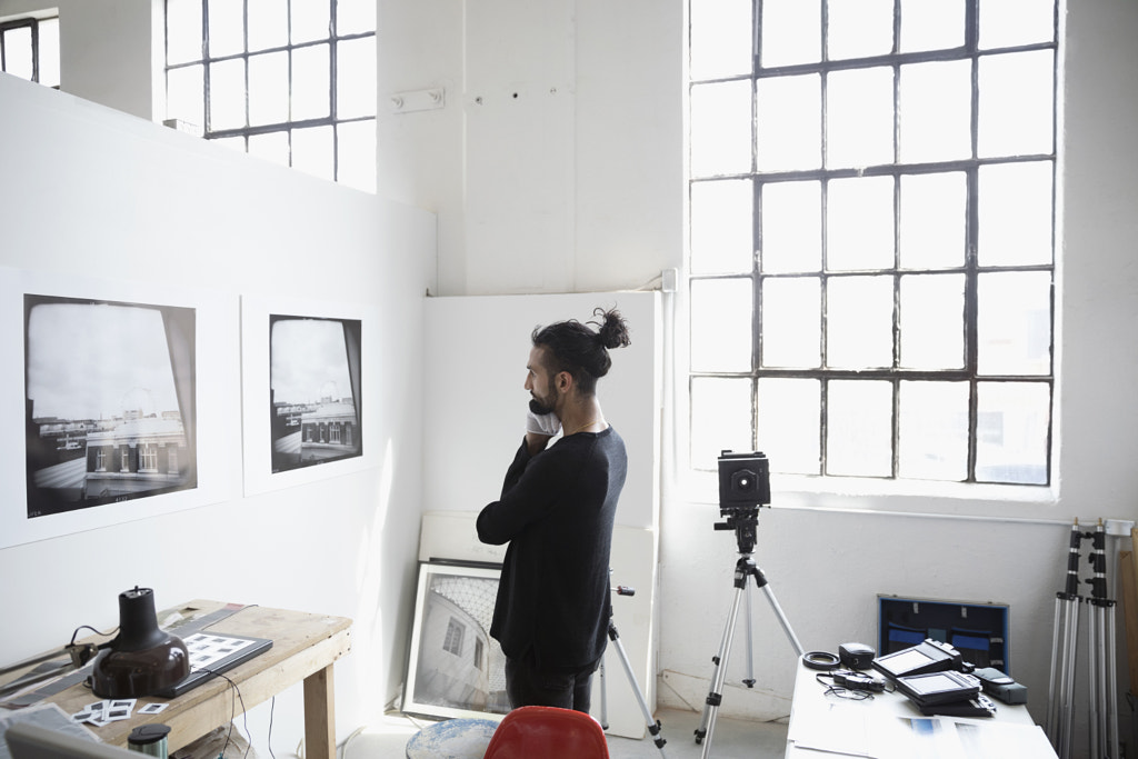 Focused male photographer examining large photography print hanging on wall in art studio by Hero Images on 500px.com