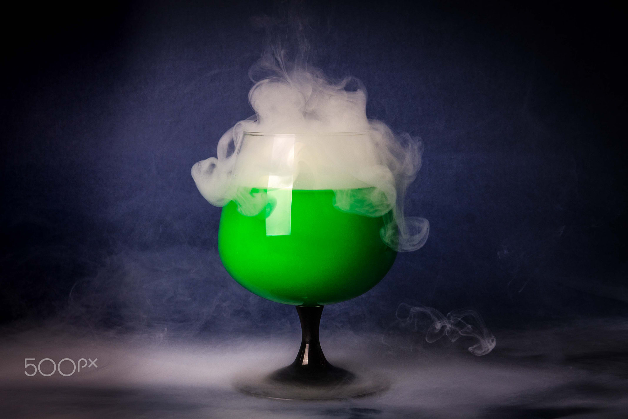 Smoke into cocktail glass on a black background. Witch potion background for Halloween. Unusual...