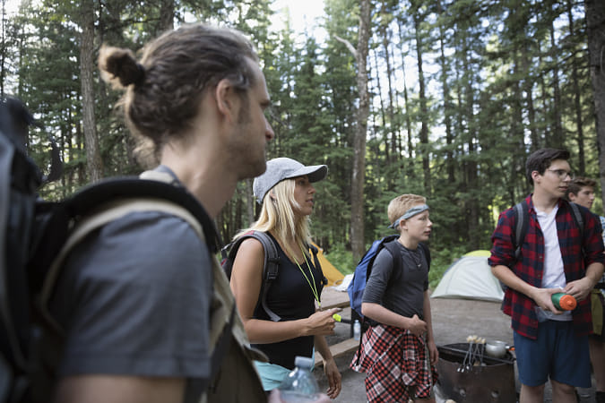 Outdoor school teachers and students looking away at campsite in woods