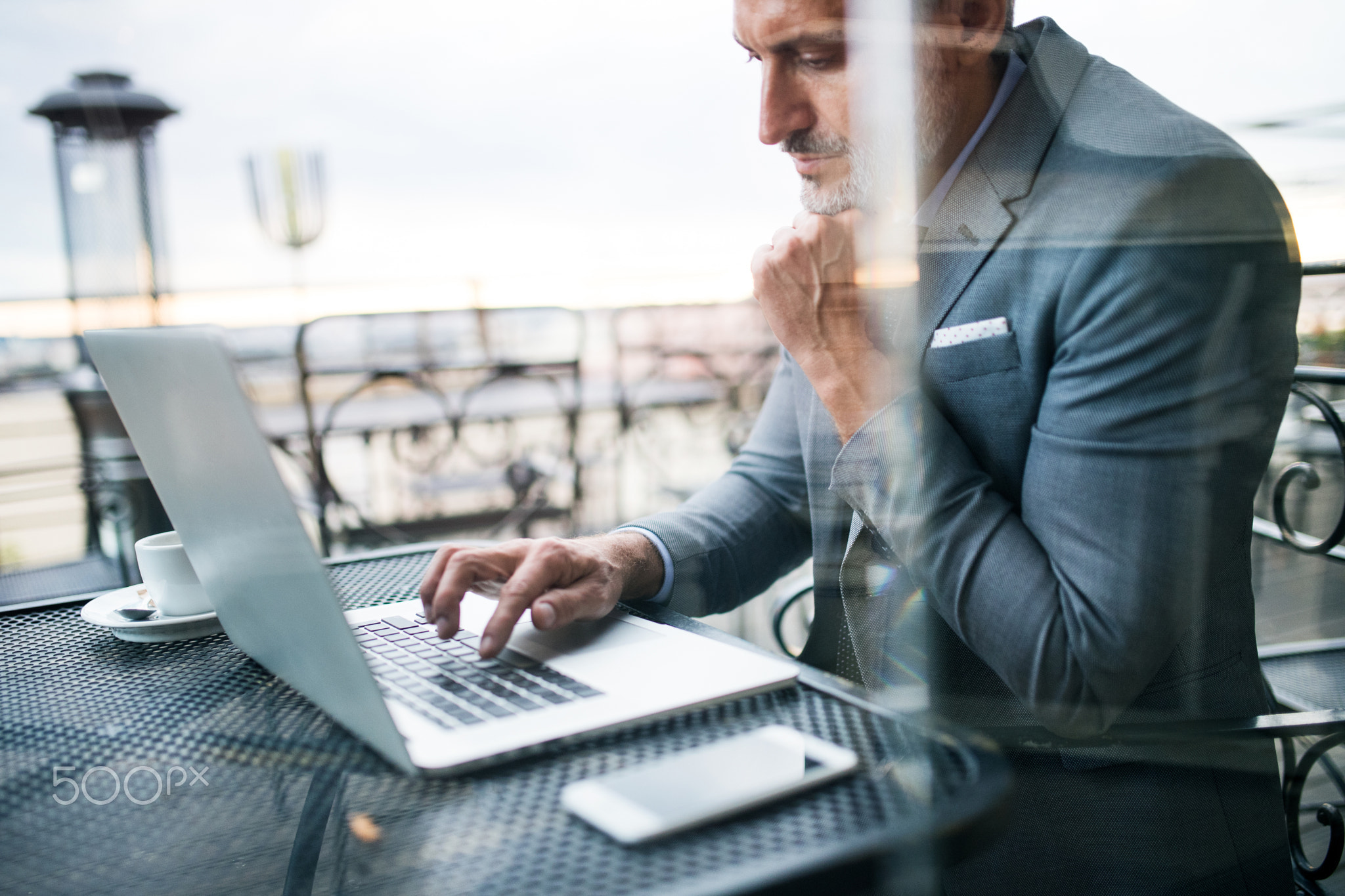 Mature businessman with laptop outside a cafe.
