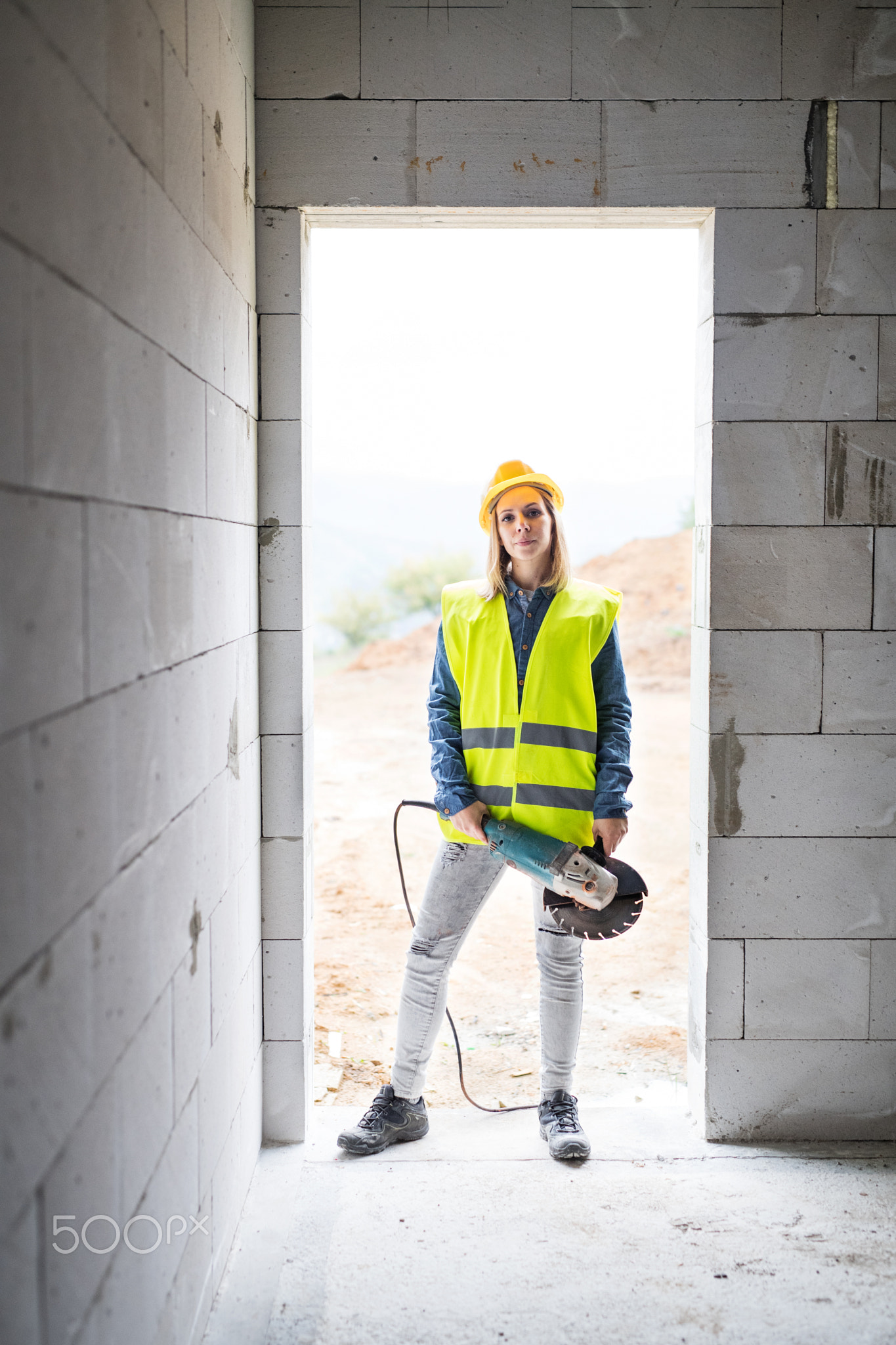 Young woman worker with electric tool on the construction site.