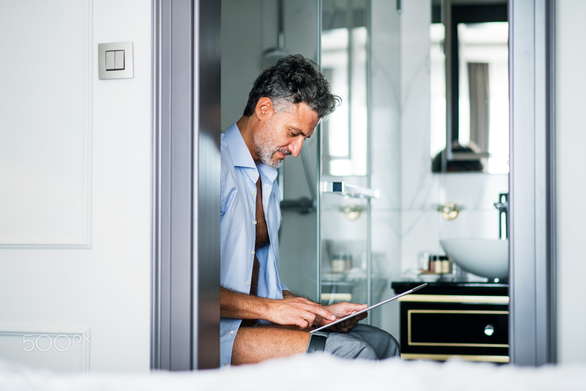 Mature businessman with tablet in a hotel room bathroom.