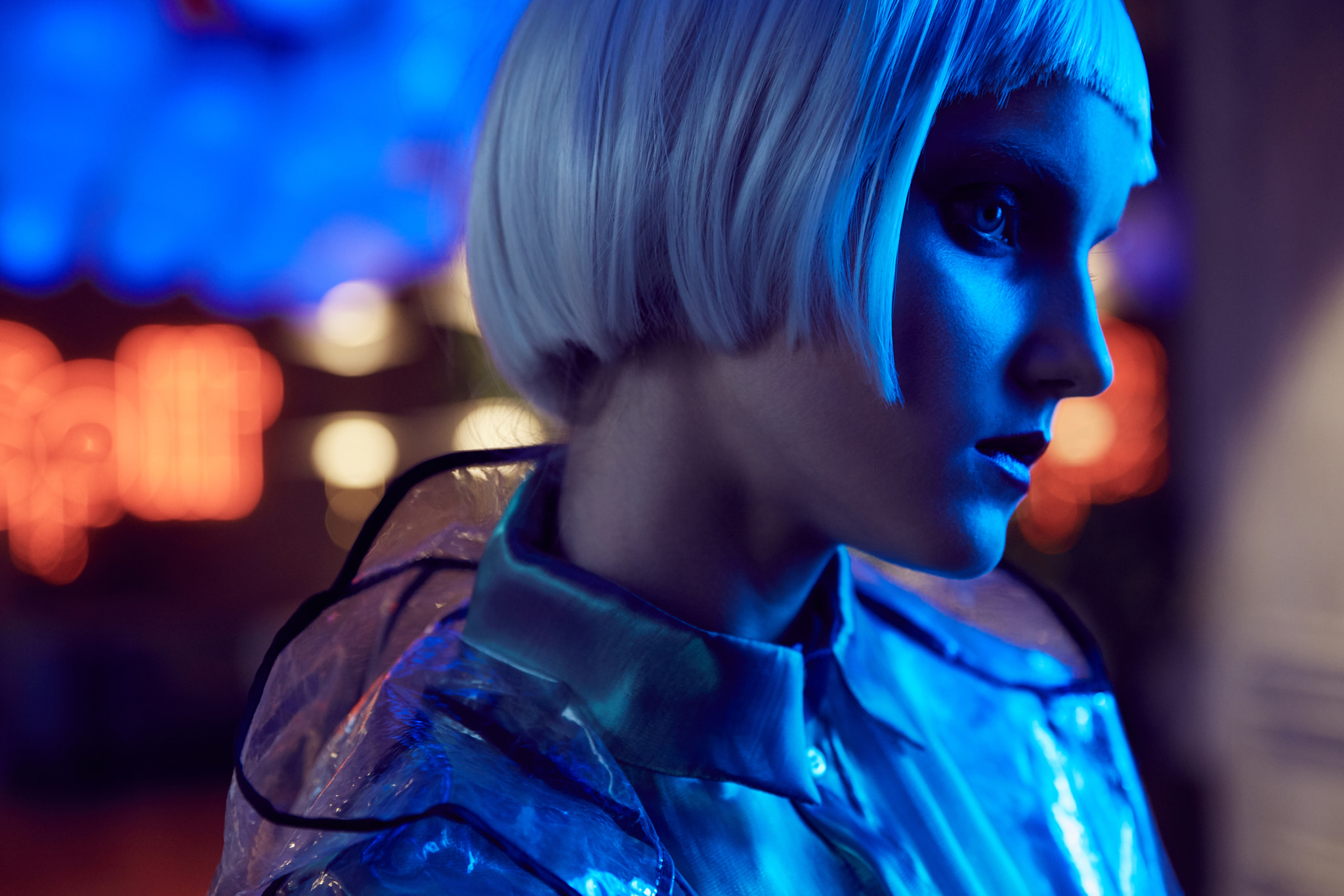Futuristic neon lighted close up portrait of a girl with white bob hairstyle wearing silky blouse...