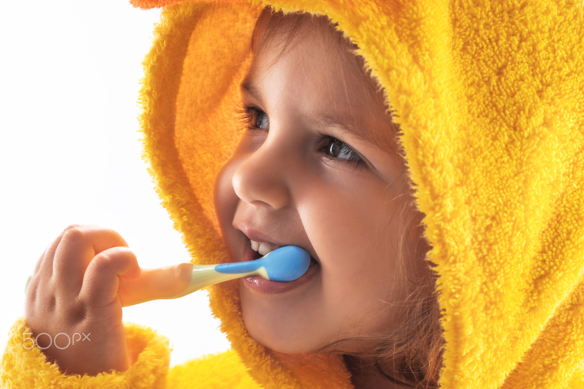 Little baby smiling under a yellow towel and brushing his teeth