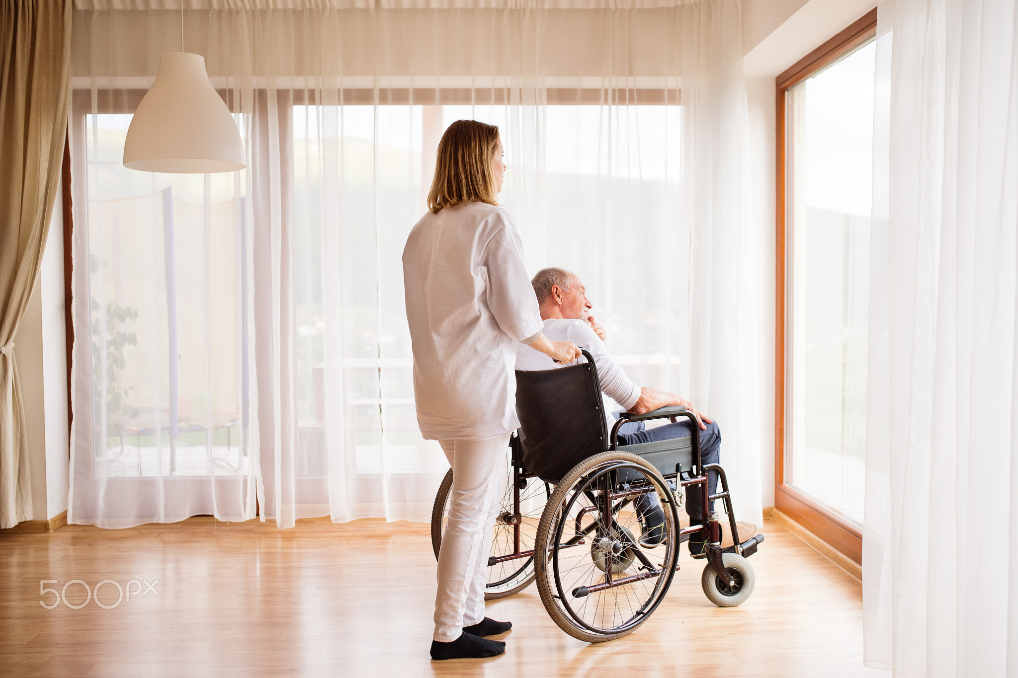 Nurse and senior man in wheelchair during home visit.