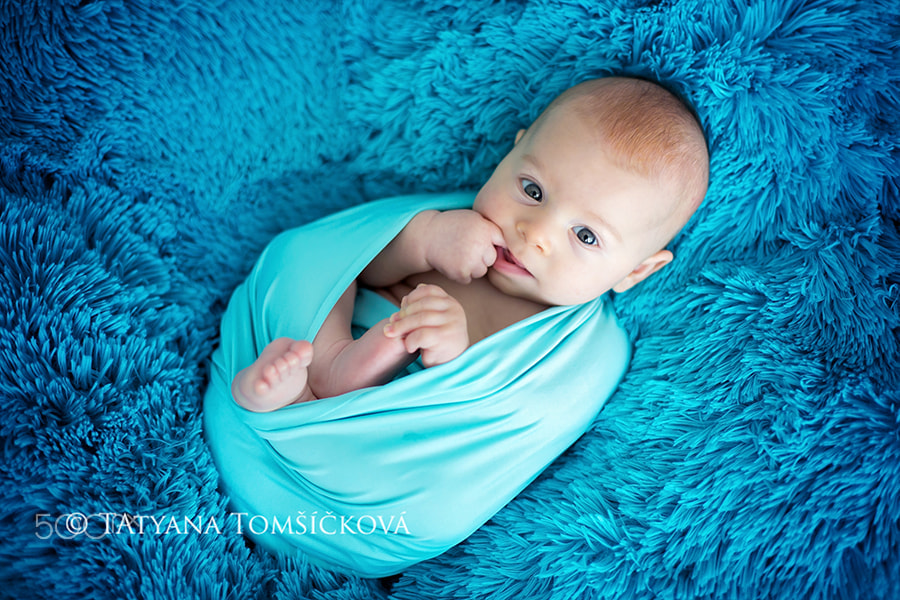 Cute three months old baby boy in blue wrap, lying on a blue bla