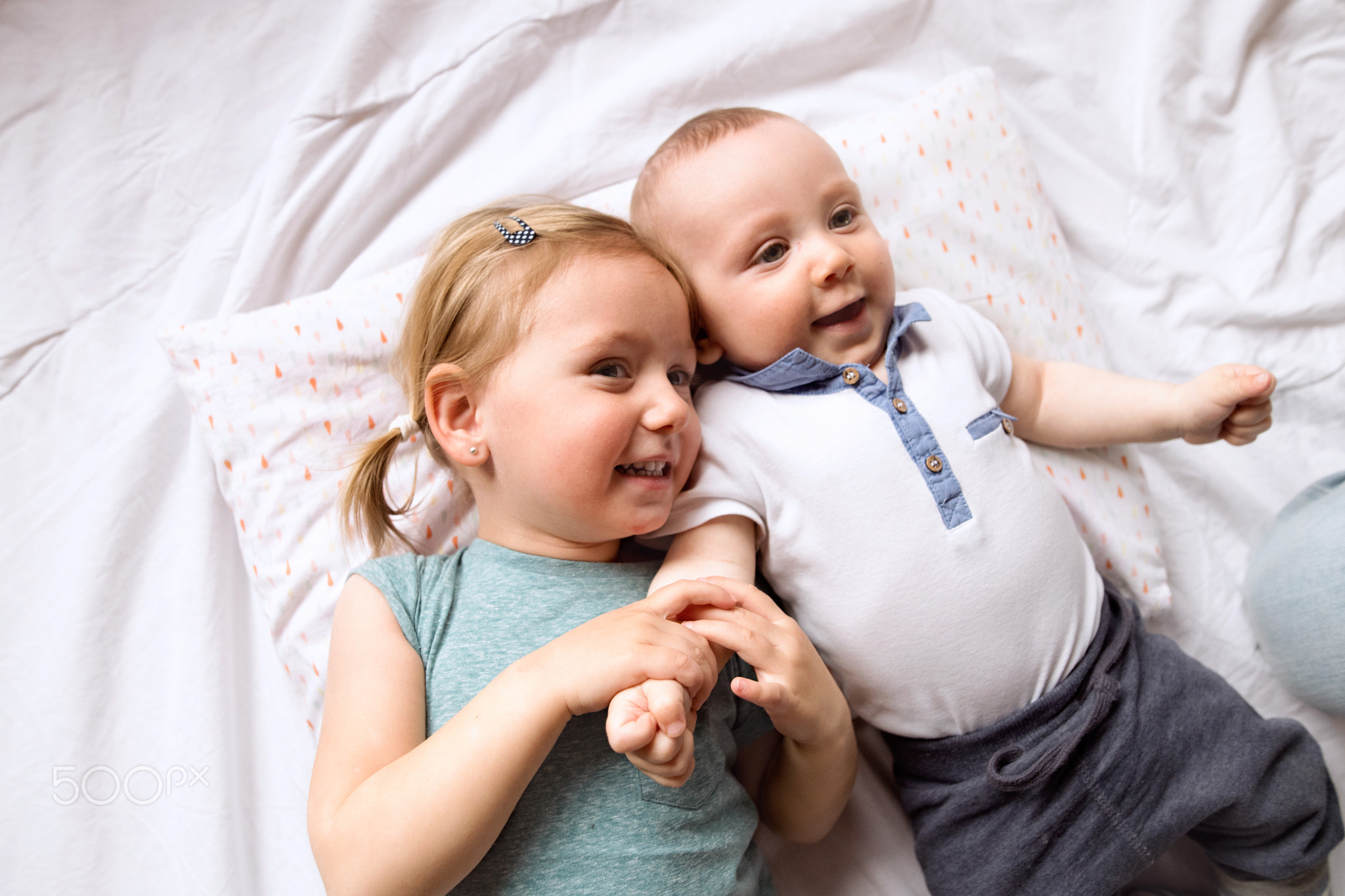 Cute little girl with her baby brother lying on bed.