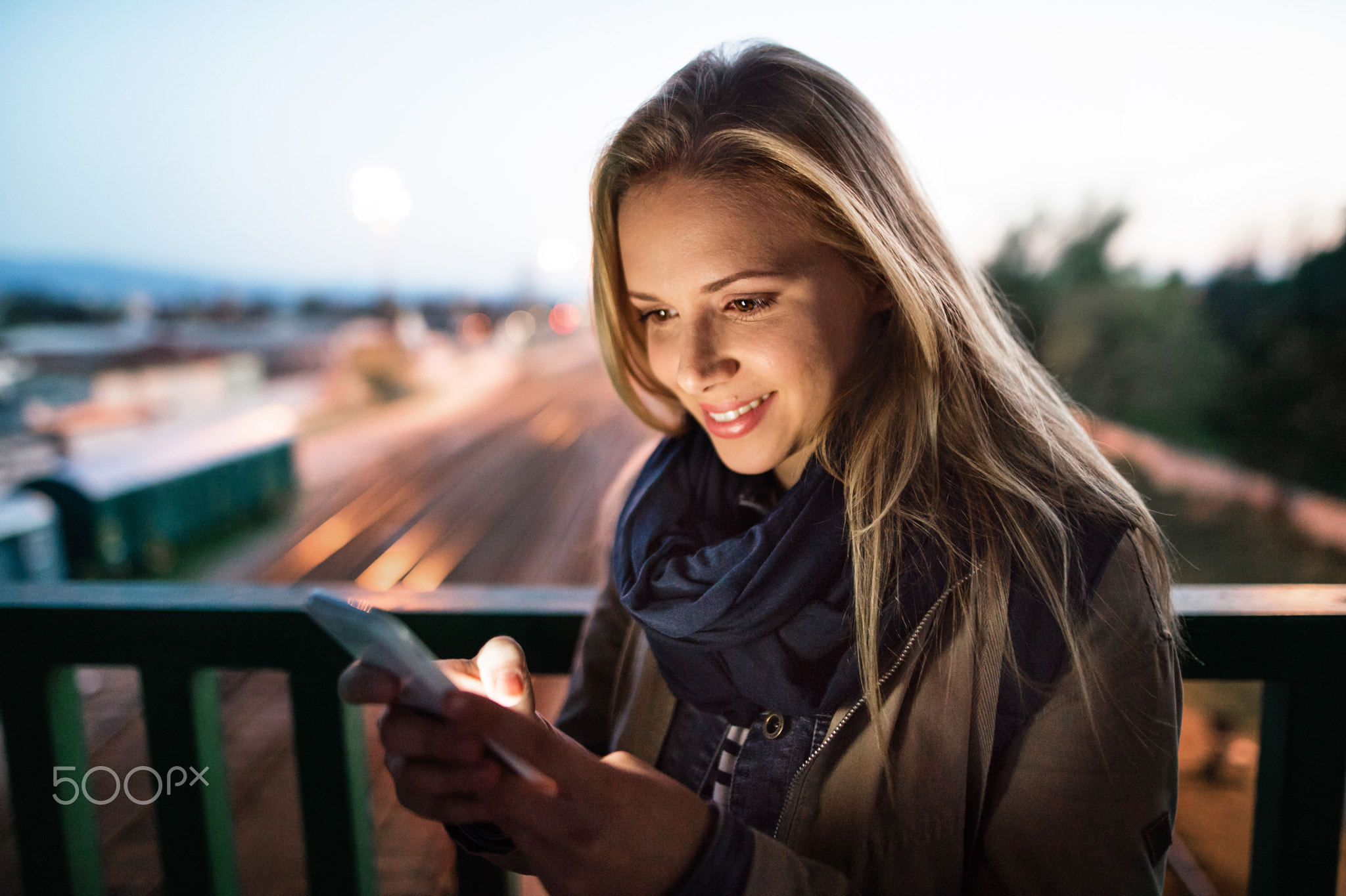 Woman in the city at night holding smartphone, texting.