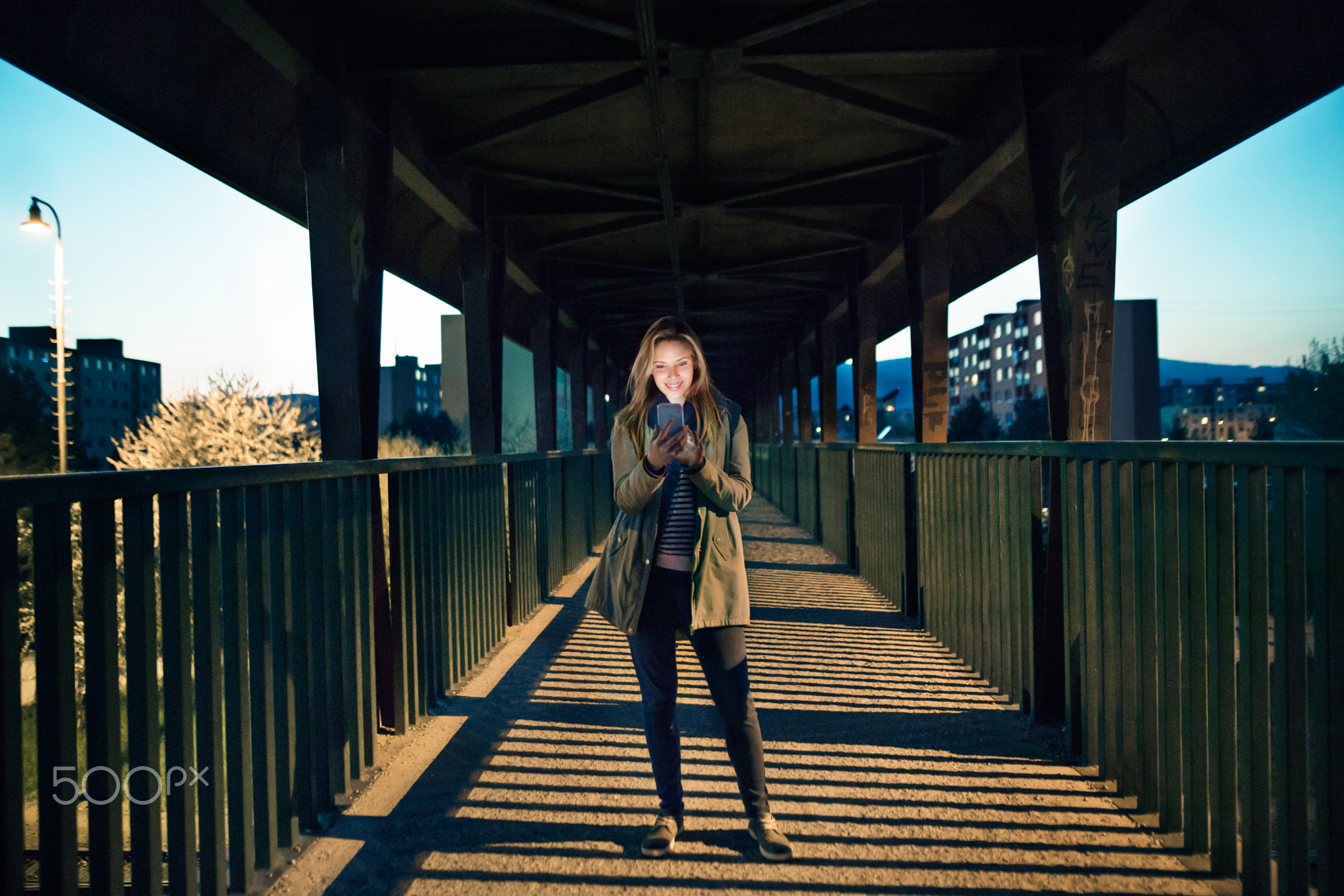 Woman in the city at night holding smartphone, texting.