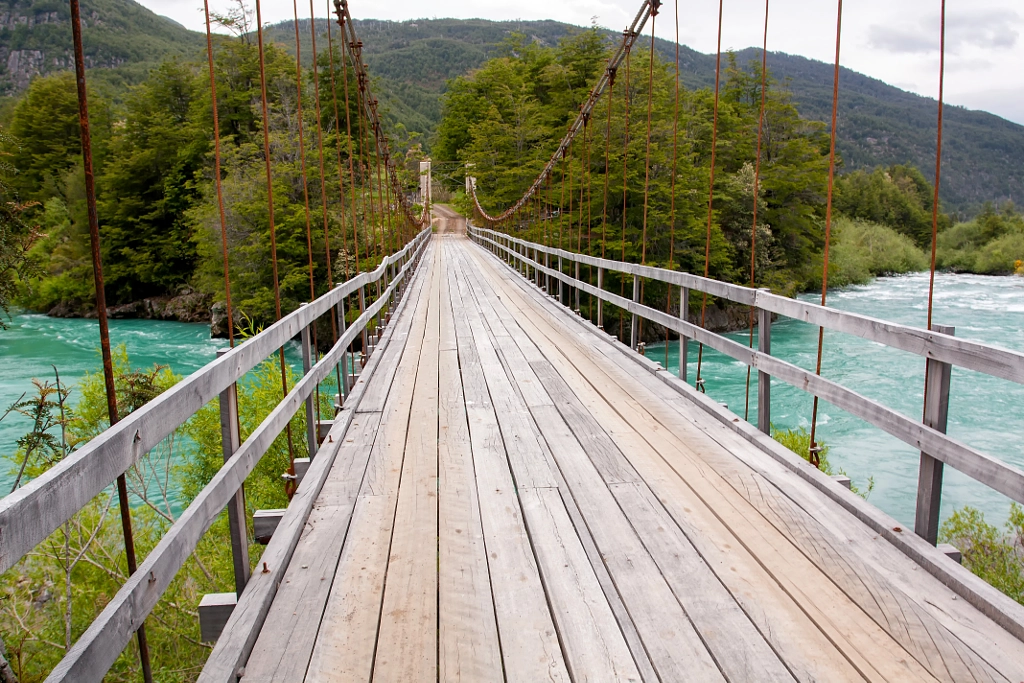 Suspended wood bridge with cables over green river