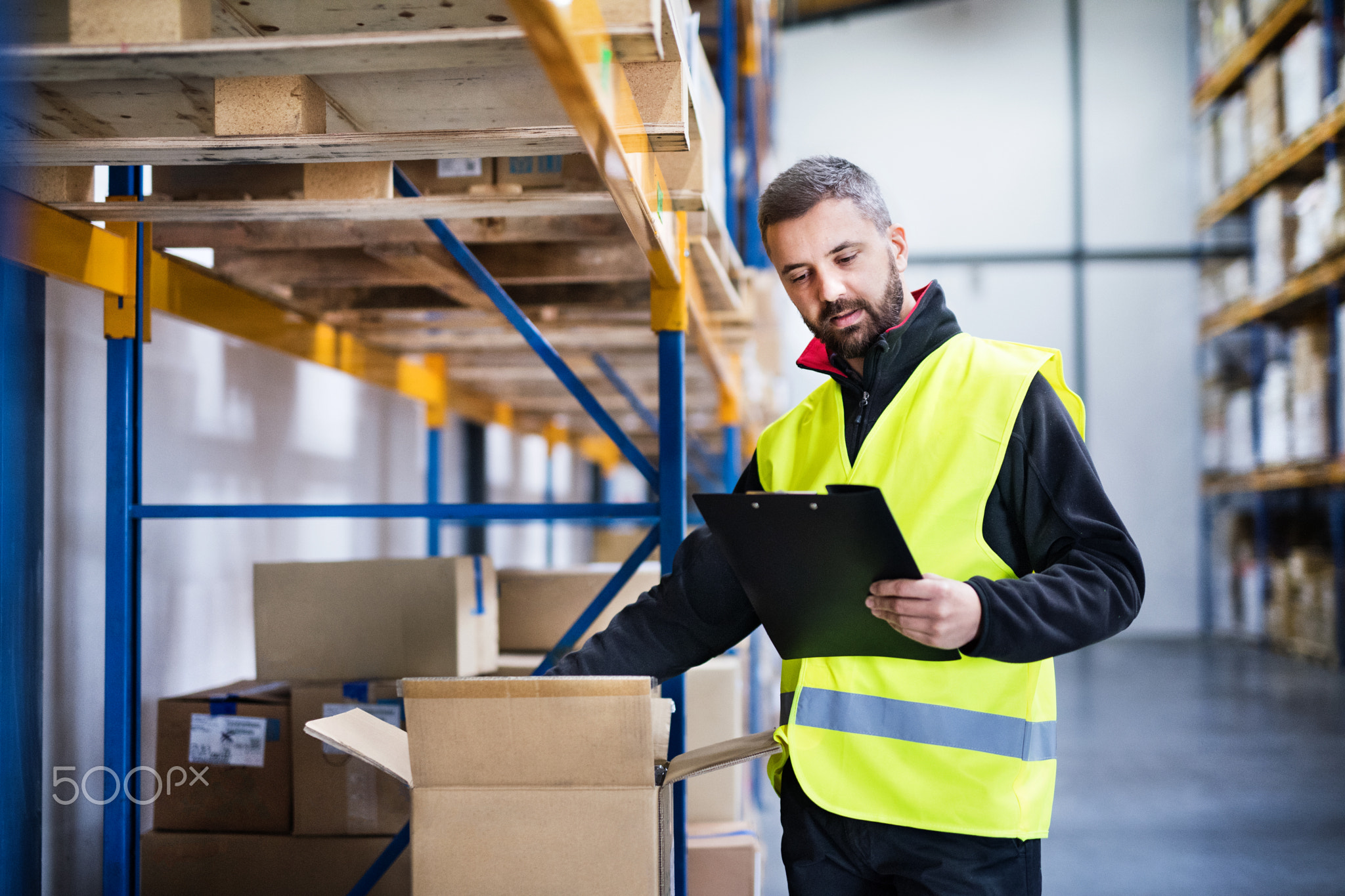 Male warehouse worker with clipboard controlling stock.