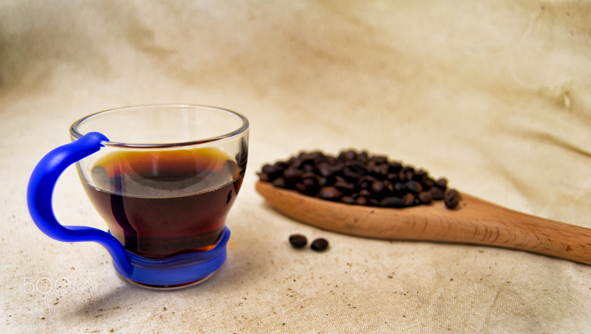 soft focus of a cup of energetic drink infusion and coffee beans on a wooden spoon with a raw...