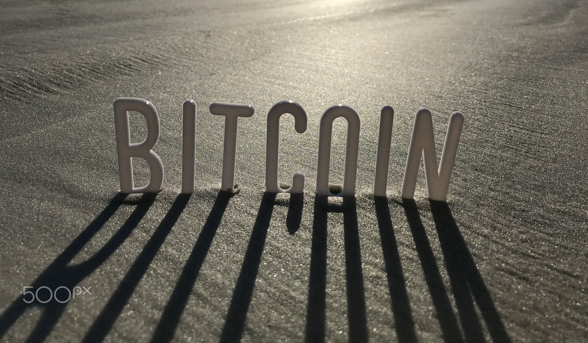 Bitcoin word in Sand with Shadows by Sun