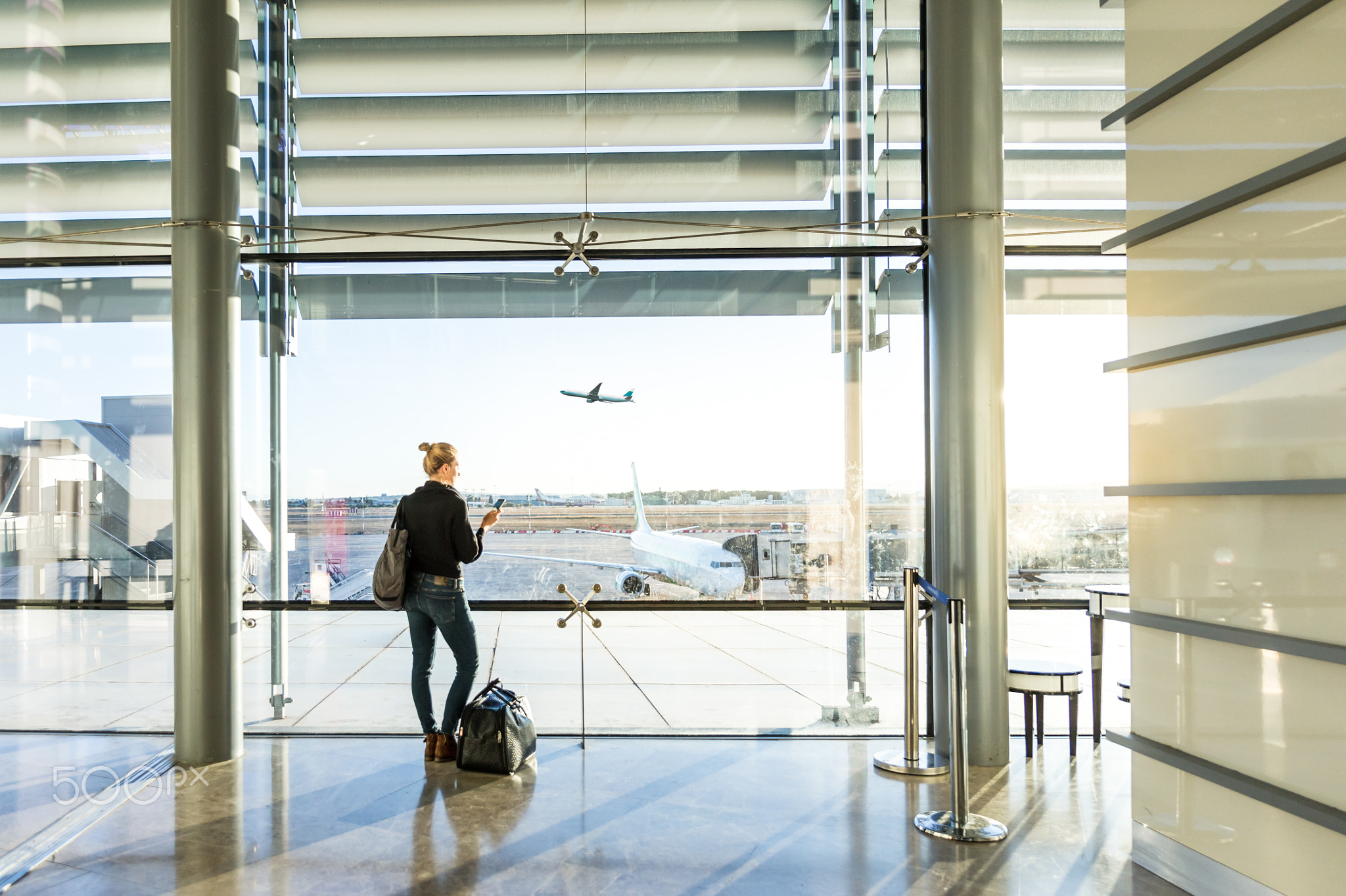 Young woman waiting at airport, looking through the gate window.