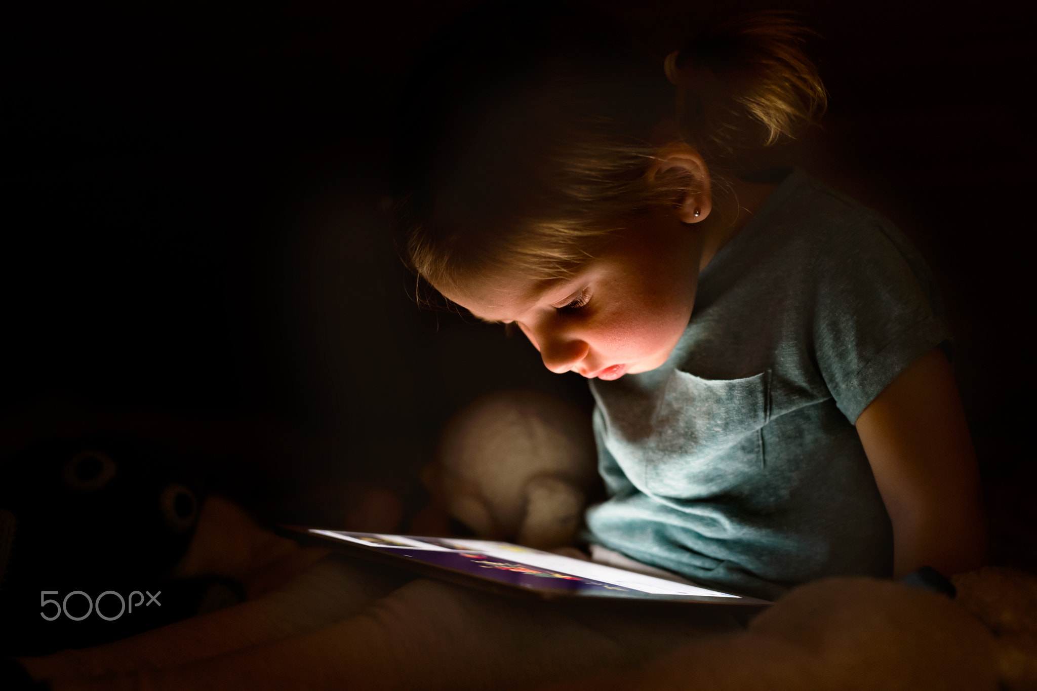 Little girl at home at night watching something on tablet.