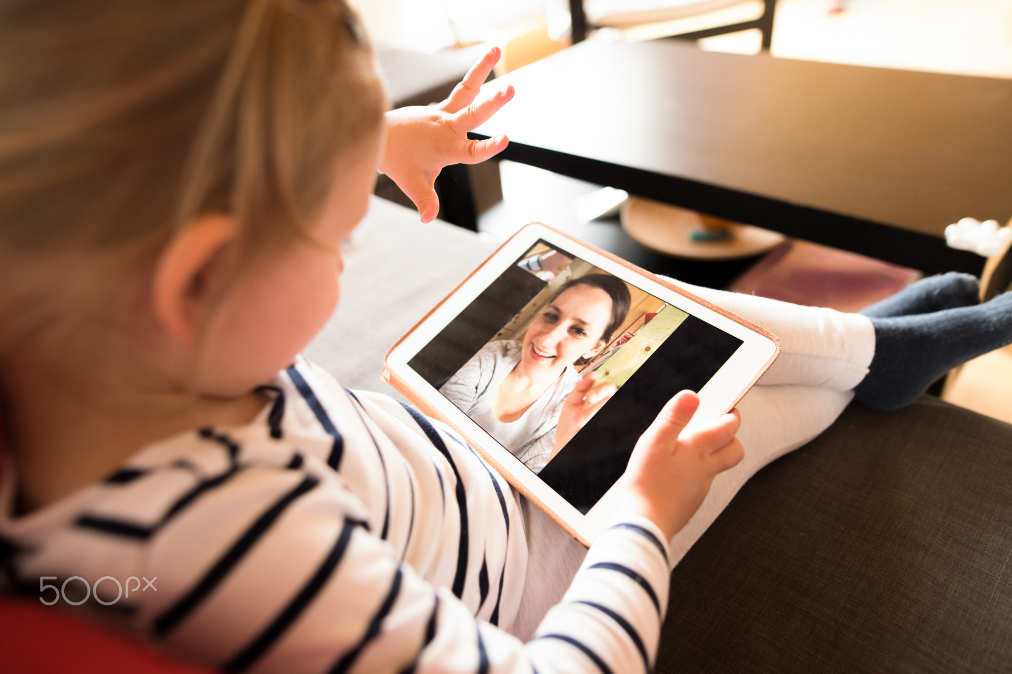 Little girl at home with tablet, video chatting with her mother.