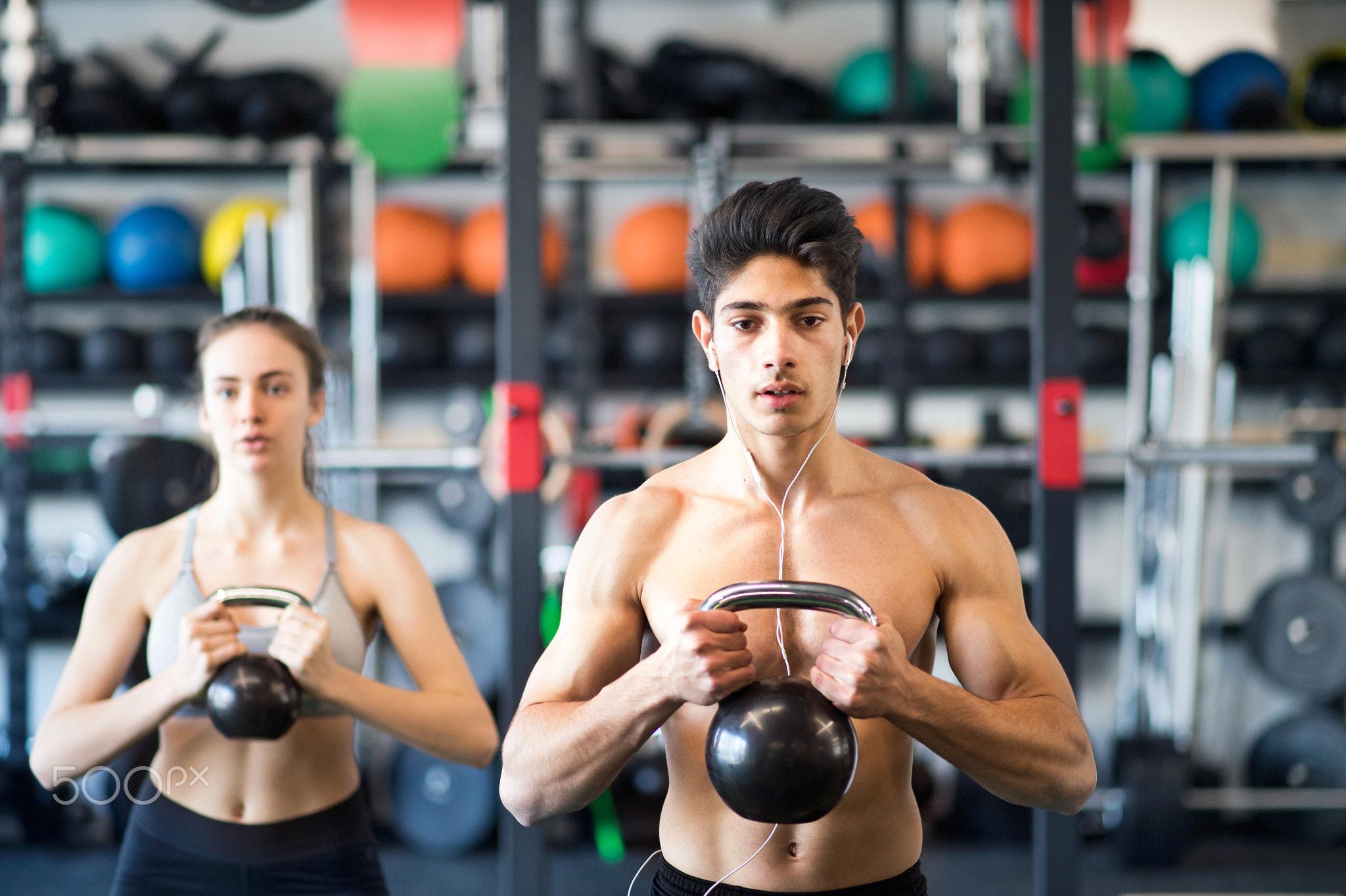 Young fit couple in gym exercising with kettlebell.