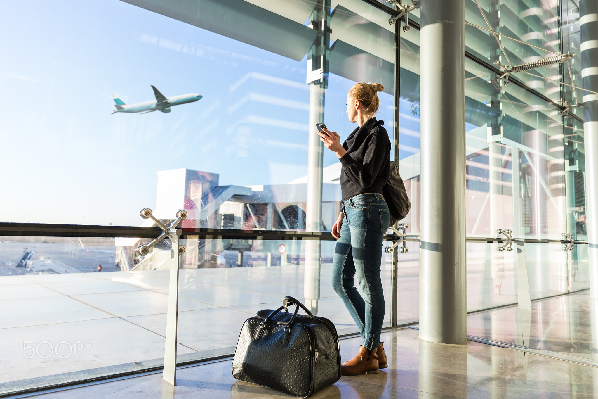 Young woman waiting at airport, looking through the gate window.