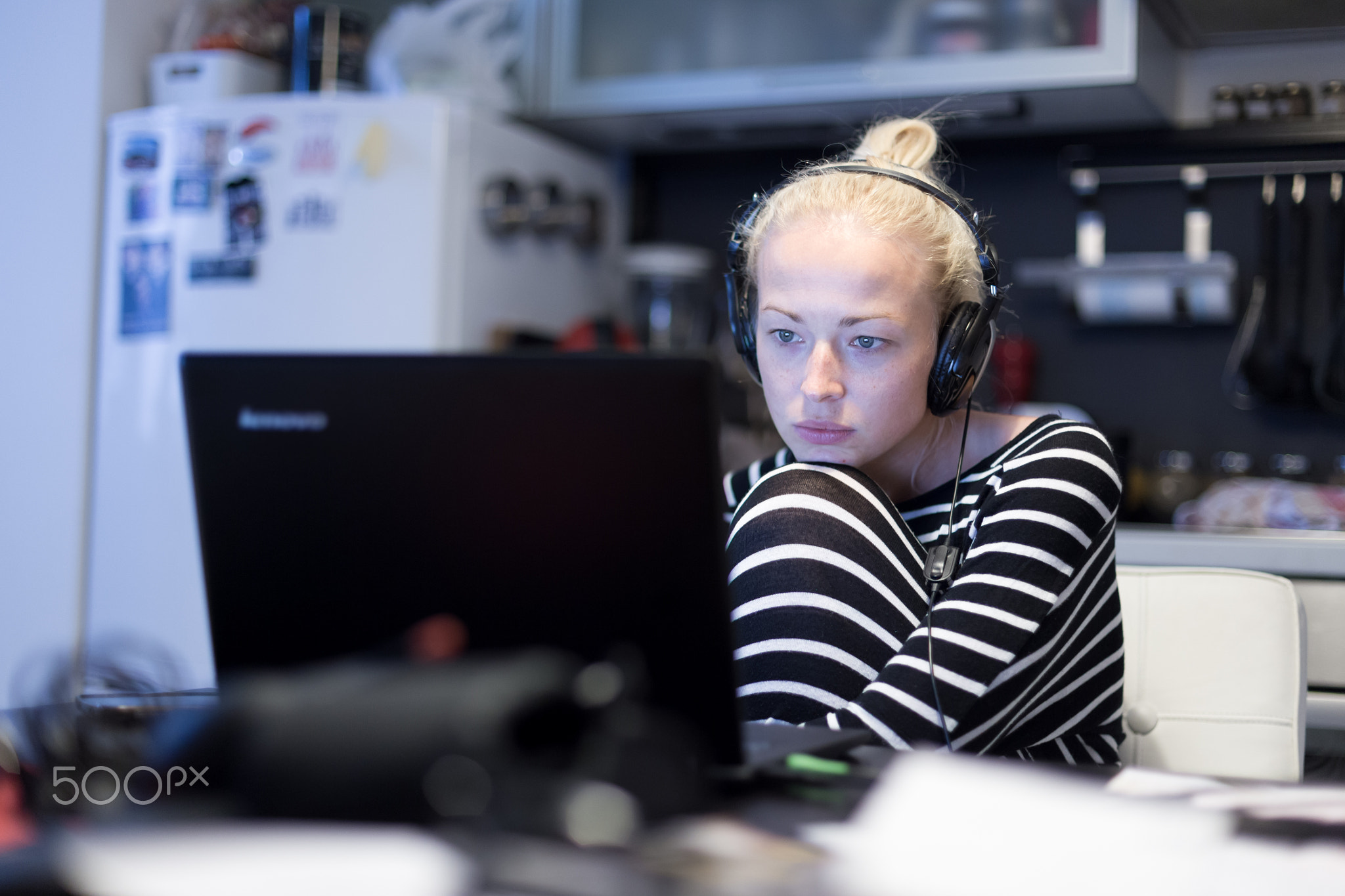 Adult woman in her casual home clothing working and studying remotely from her small flat late at...