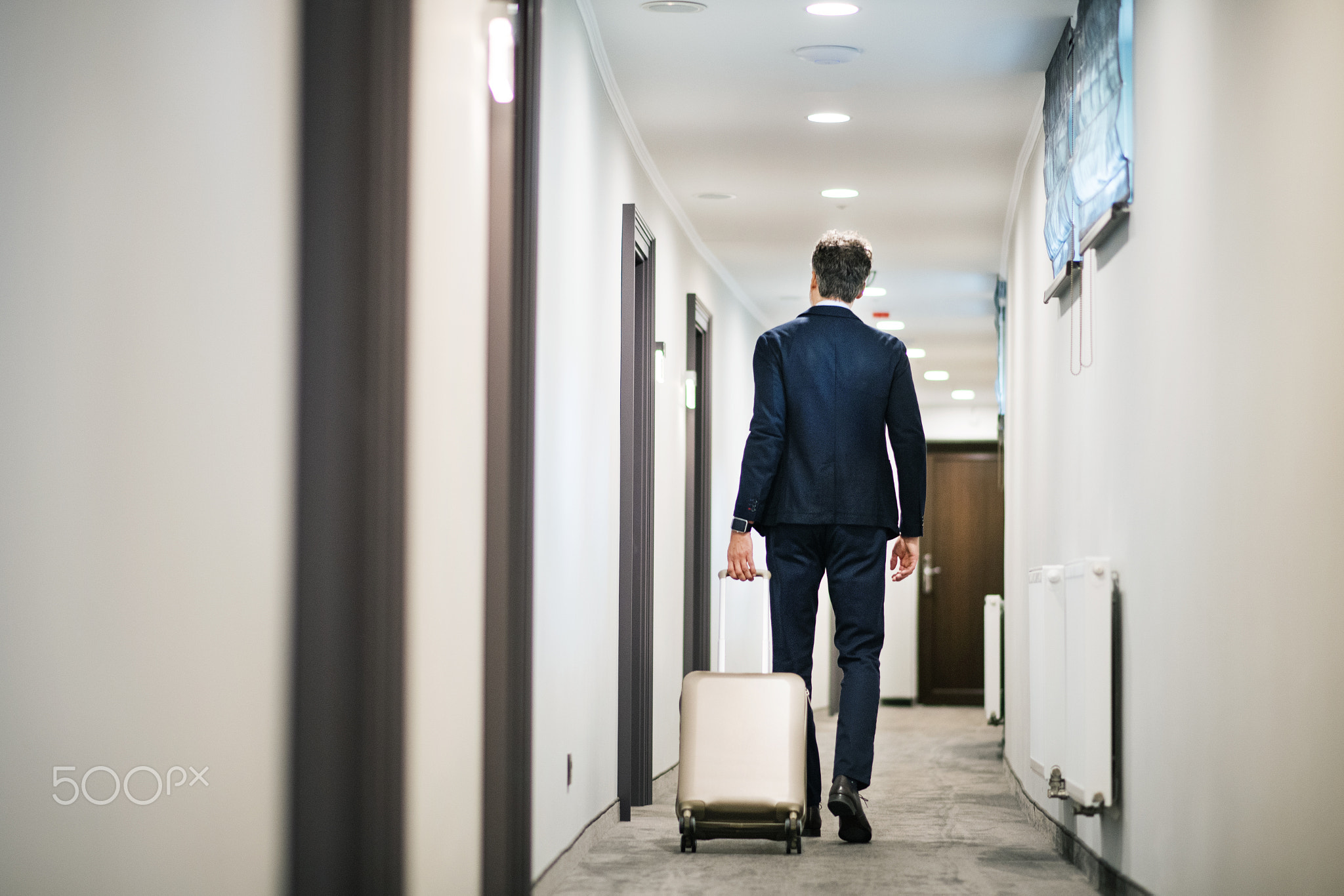 Mature businessman walking with luggage in a hotel corridor.