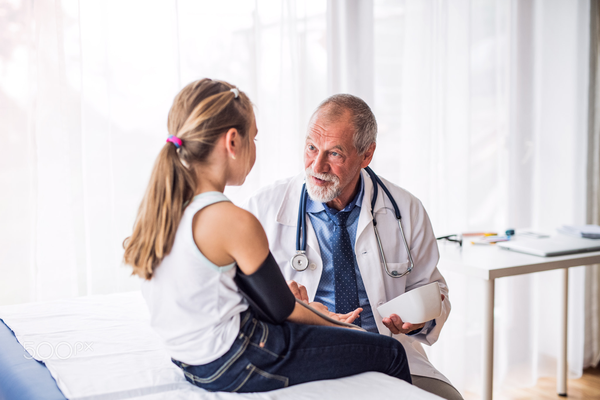 Senior doctor checking a small girl in his office.