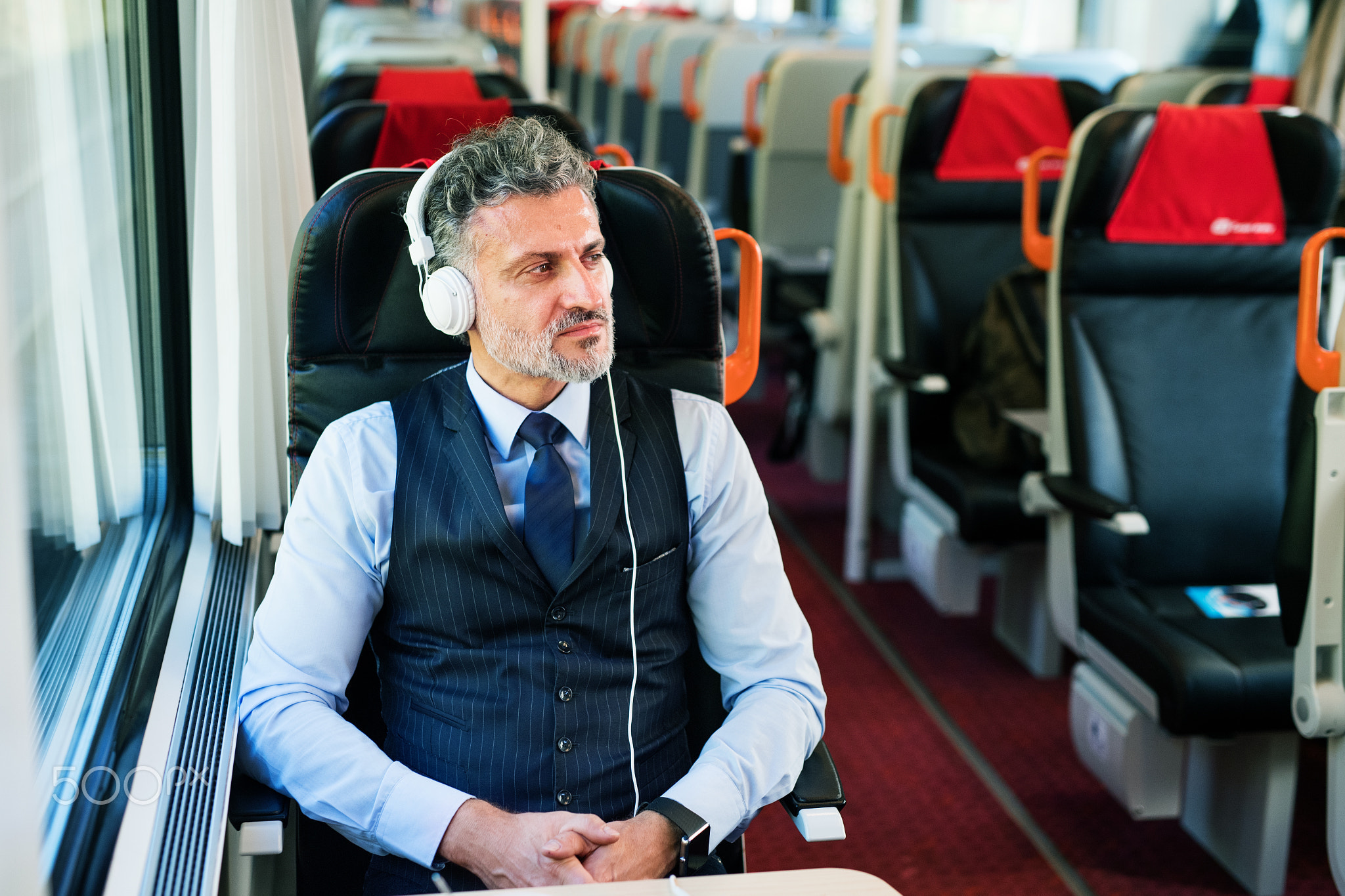 Mature businessman with headphones travelling by train.