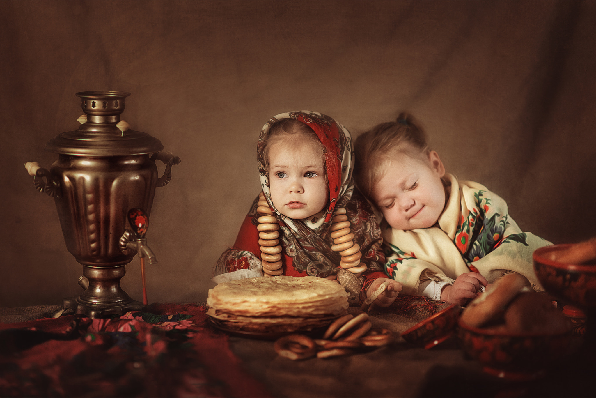 Portrait of two little girls in national costumes with pancakes, pastries and tea
