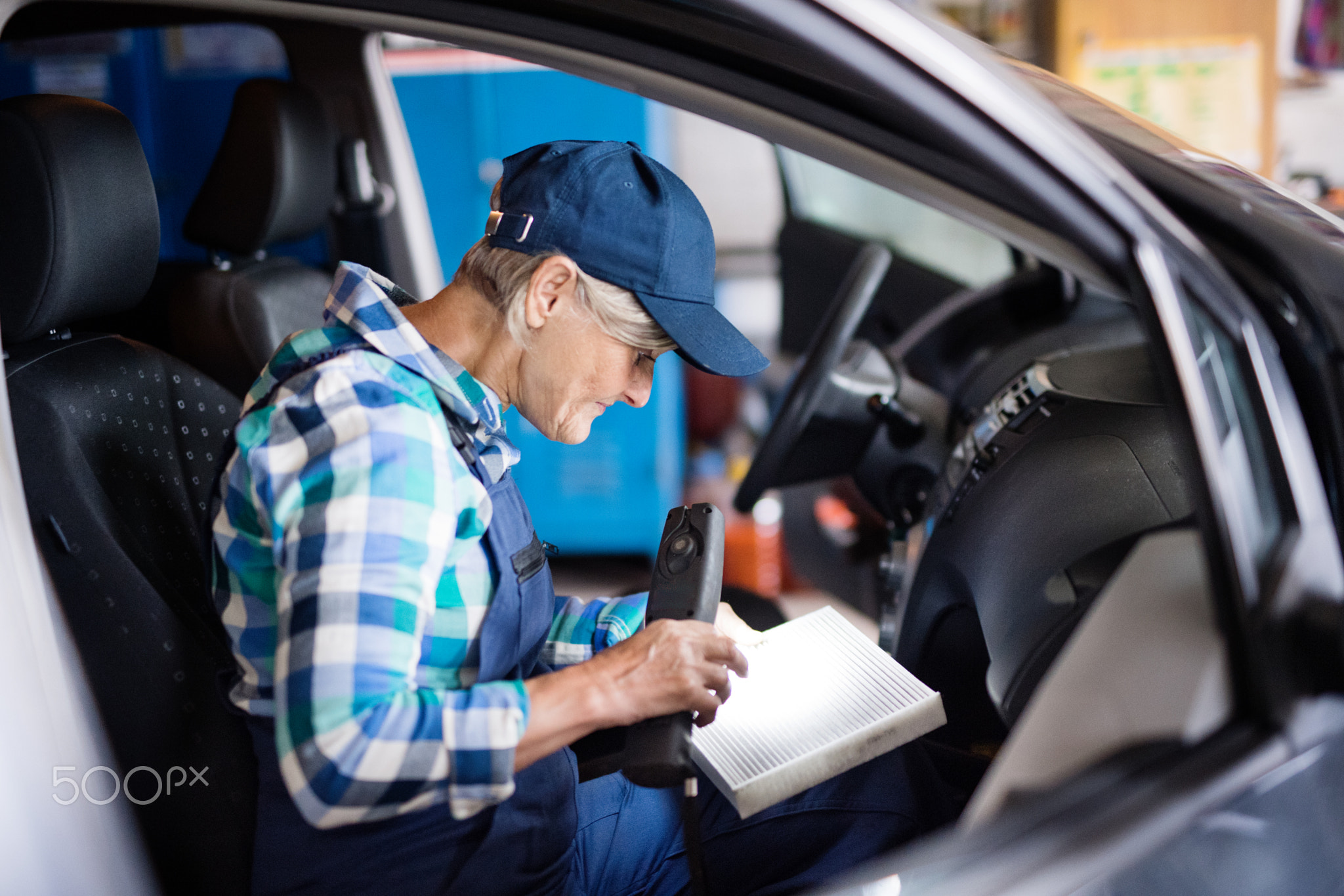 Senior female mechanic repairing a car in a garage.