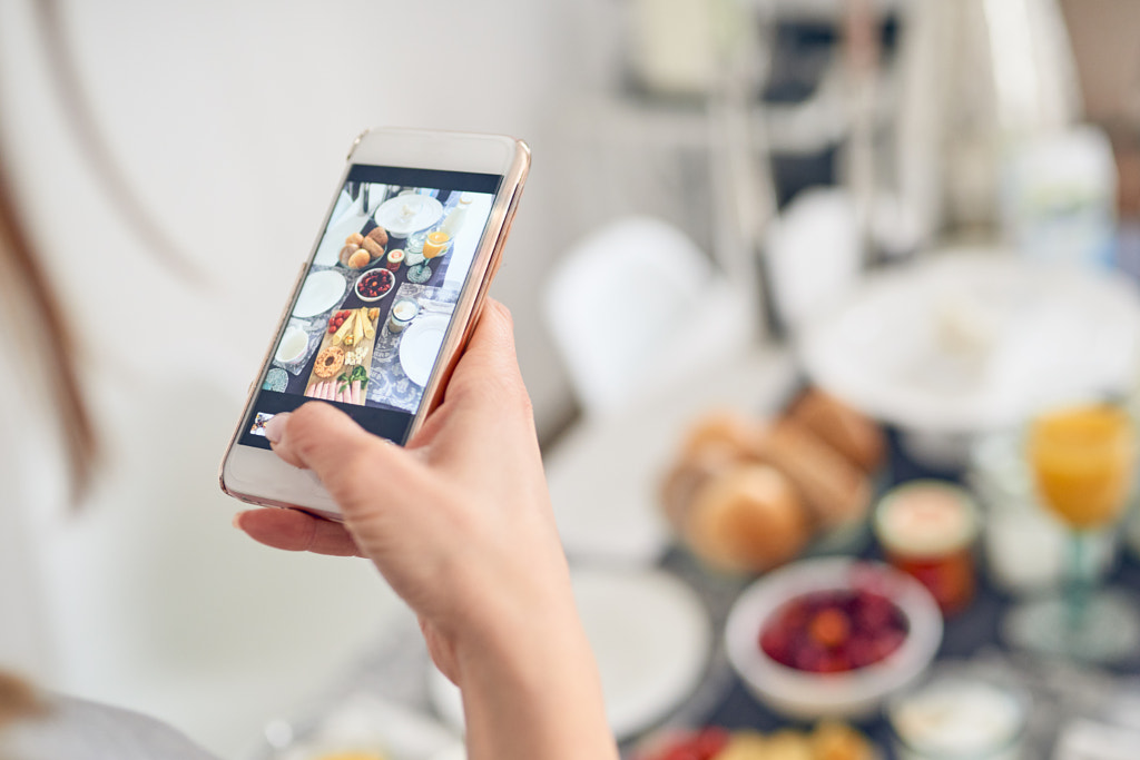 Woman taking a picture of her breakfast with her mobile phone by Lars Zahner on 500px.com