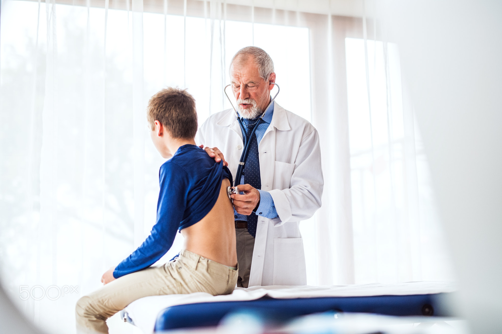 Senior doctor examining a small boy in his office.