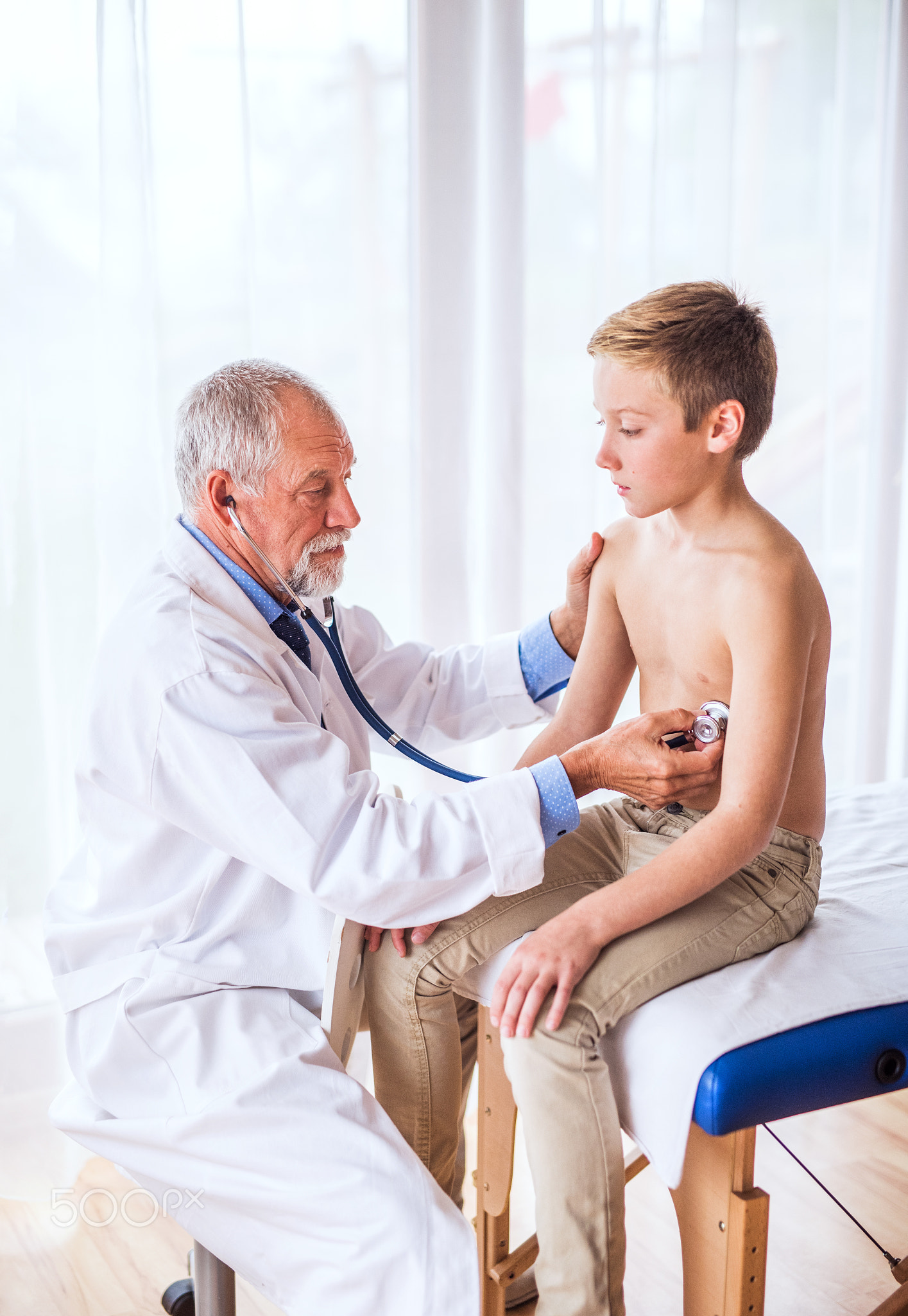 Senior doctor examining a small boy in his office.