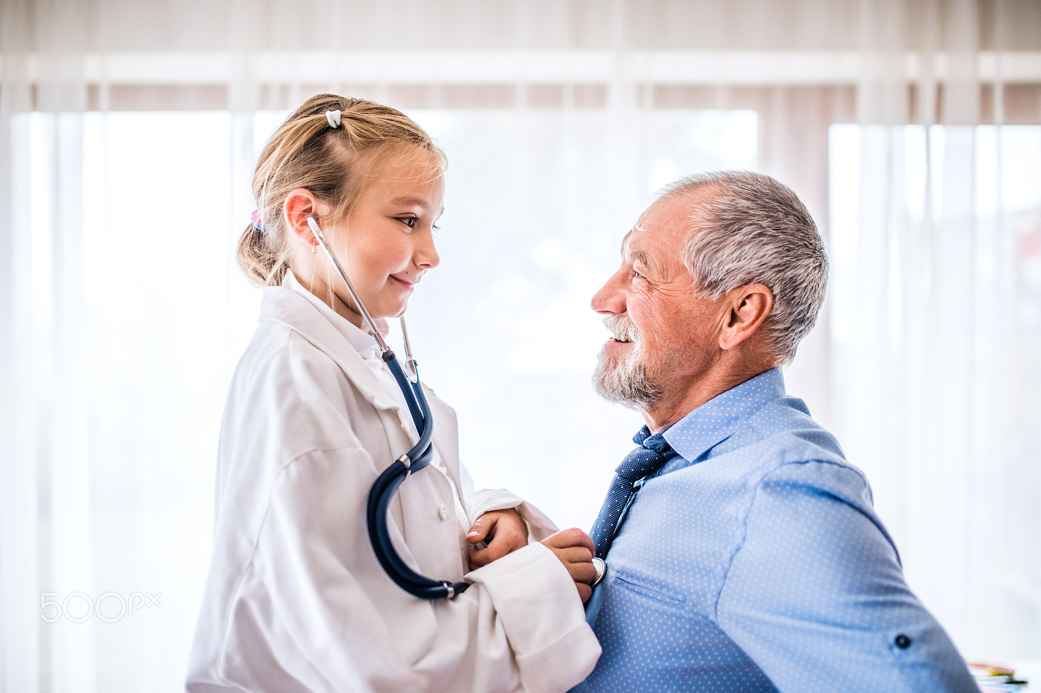 Senior doctor and a small girl with stethoscope in his office.