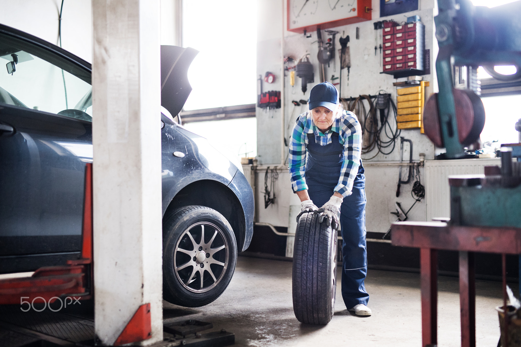 Senior female mechanic repairing a car in a garage.