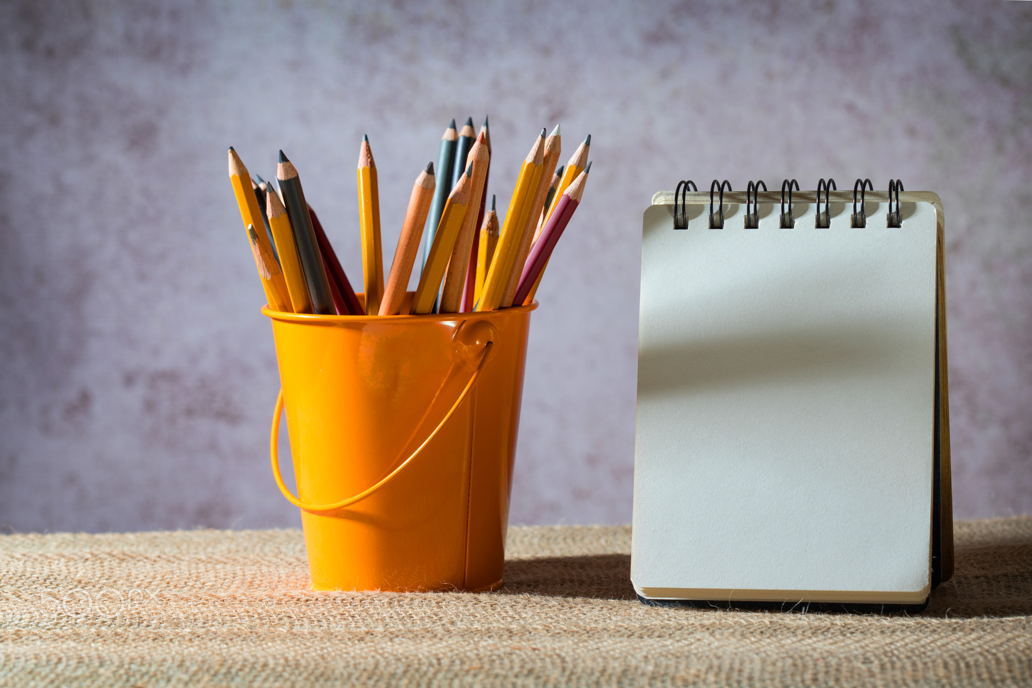 A set of colored pencils on a toy bucket and a blank small notebook