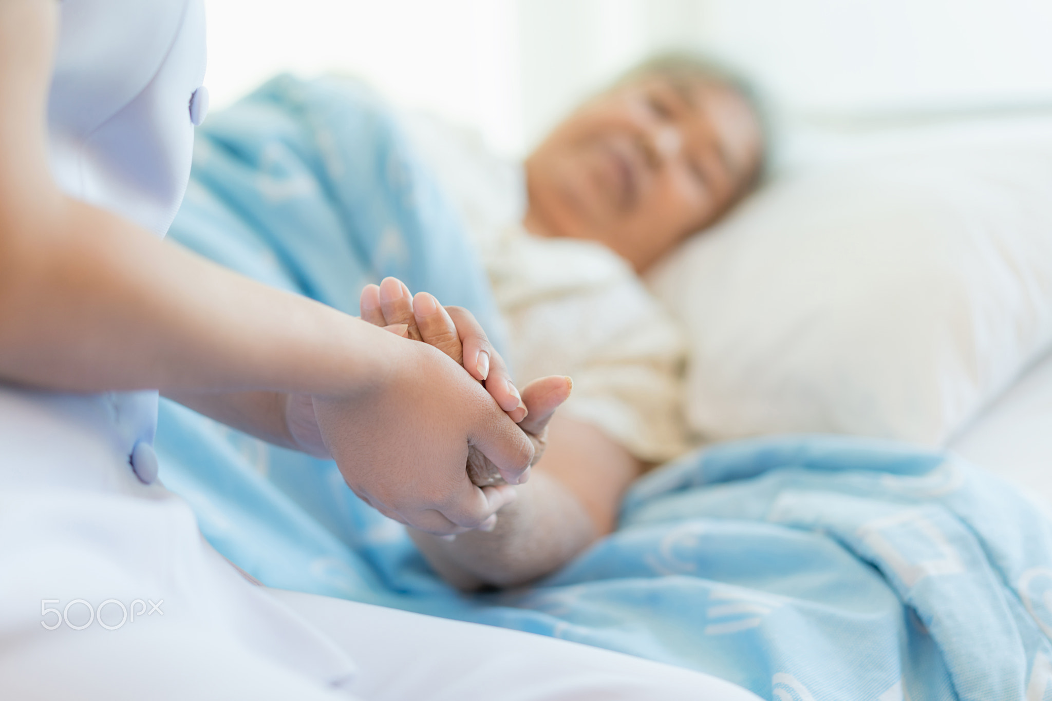 Nurse sitting on a hospital bed next to an older woman helping h