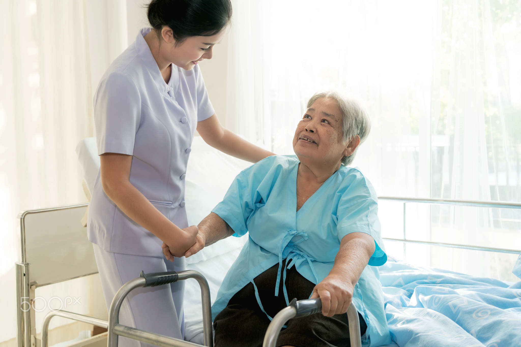 Asian young nurse supporting elderly patient disabled woman in u