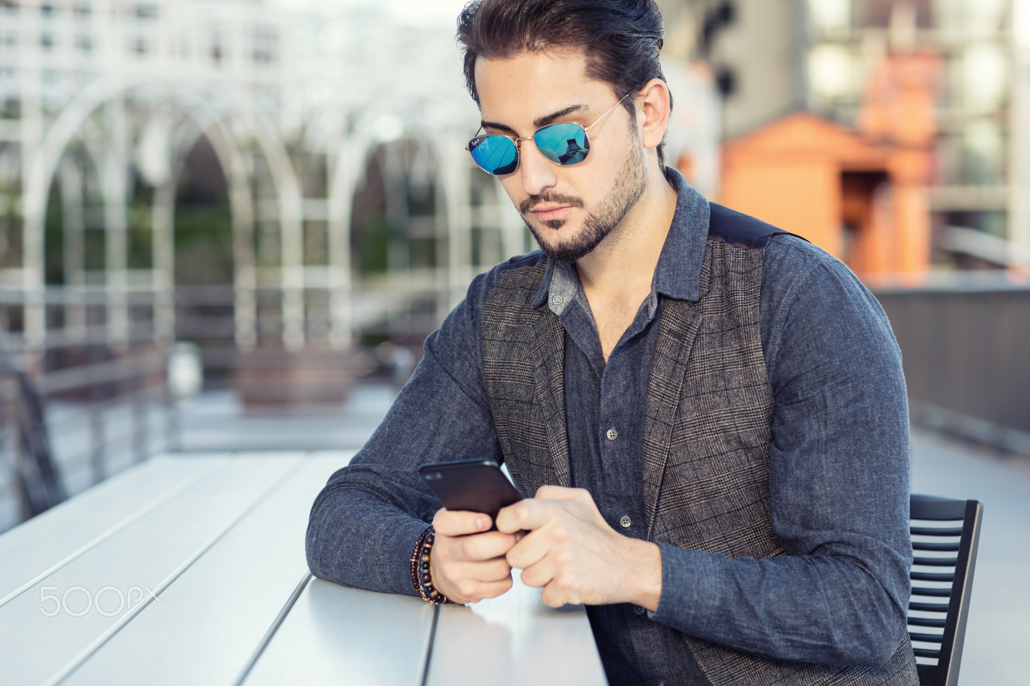 A young handsome man in sunglasses texting on his phone outdoors