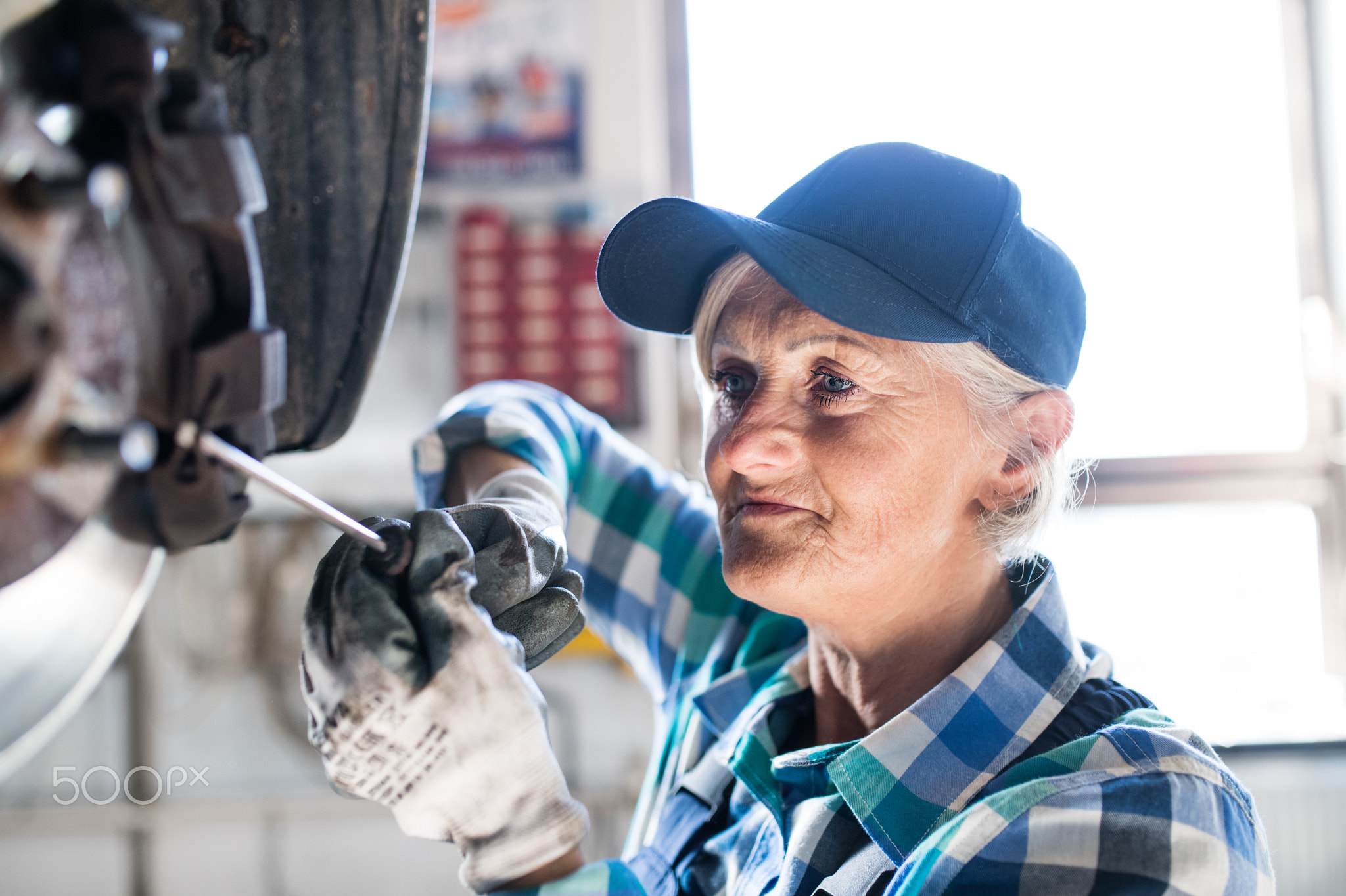 Senior female mechanic repairing a car in a garage.