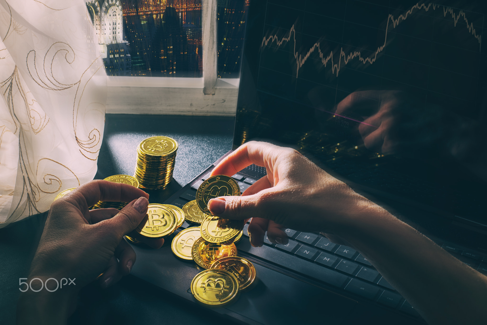 A stack of bitcoins by the laptop. Beautiful view of New York skyscrapers in the window.