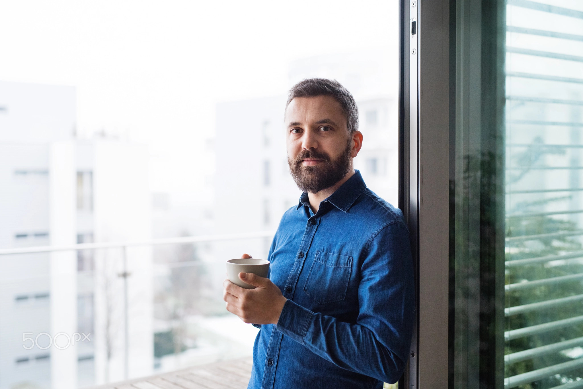 A man by the window holding a cup of coffee at home.